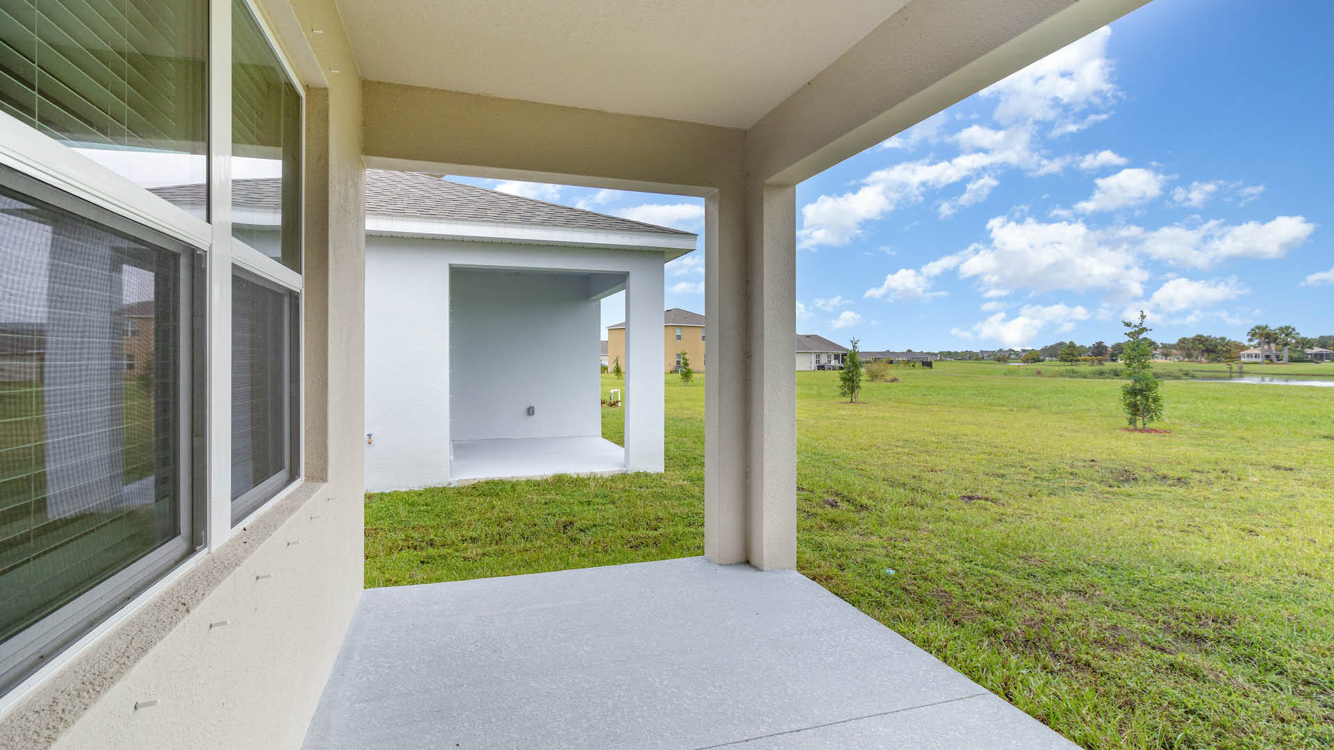 A rear view of a house featuring a stucco exterior, covered patio and well-kept lawn.