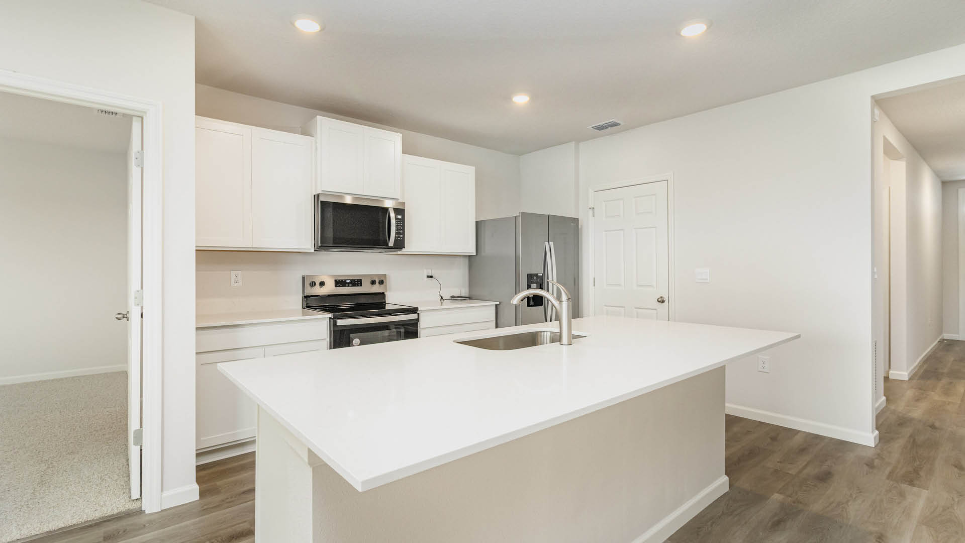 Modern kitchen with white cabinets, stainless steel appliances, and a large island; bright, open layout with a welcoming hallway.