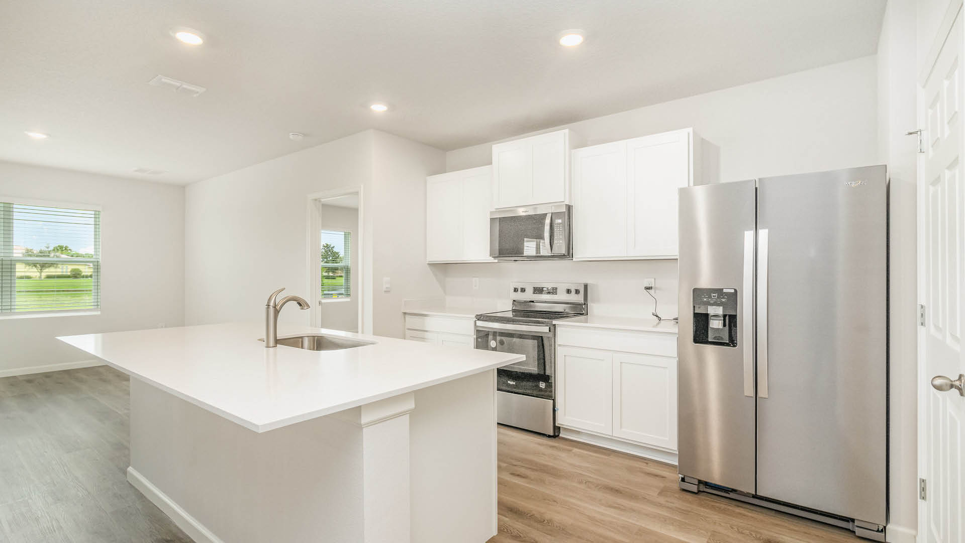 A bright, modern kitchen features white cabinetry and countertops, a central island with a built-in sink, and stainless steel appliances including a side-by-side refrigerator, stove, and over-the-range microwave.