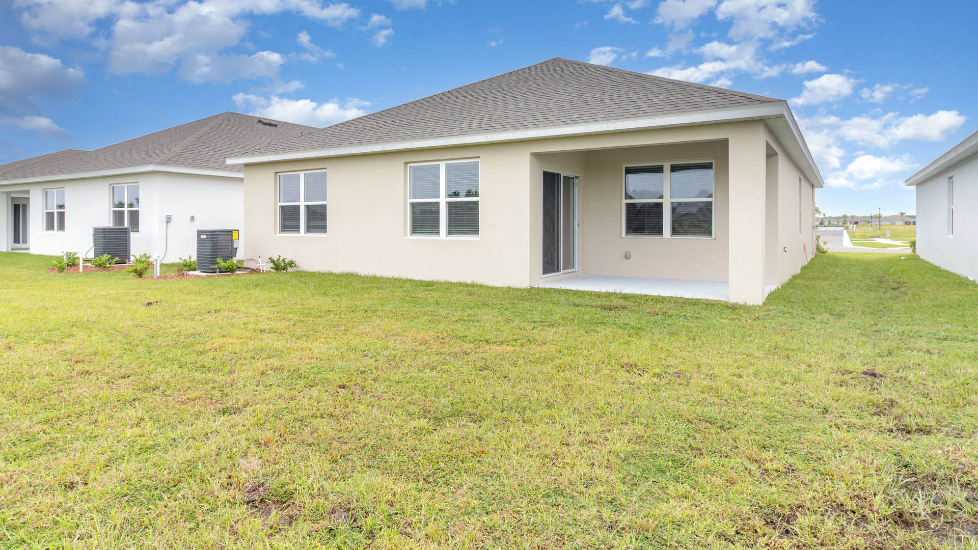 Rear view of a house featuring a white stucco exterior, covered patio, and a well-kept lawn with greenery and AC unit.