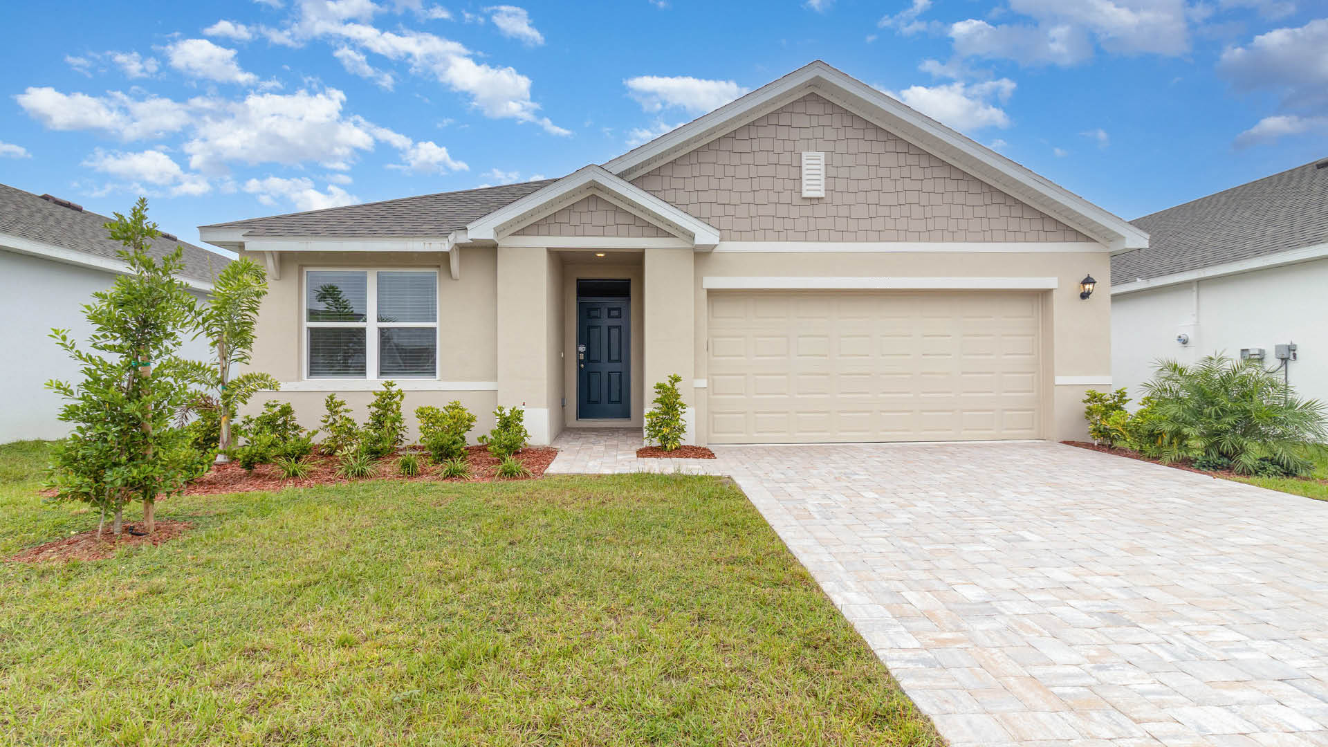 A modern single-family home with a beige and gray exterior features a paved driveway leading to a two-car garage and a blue front door.