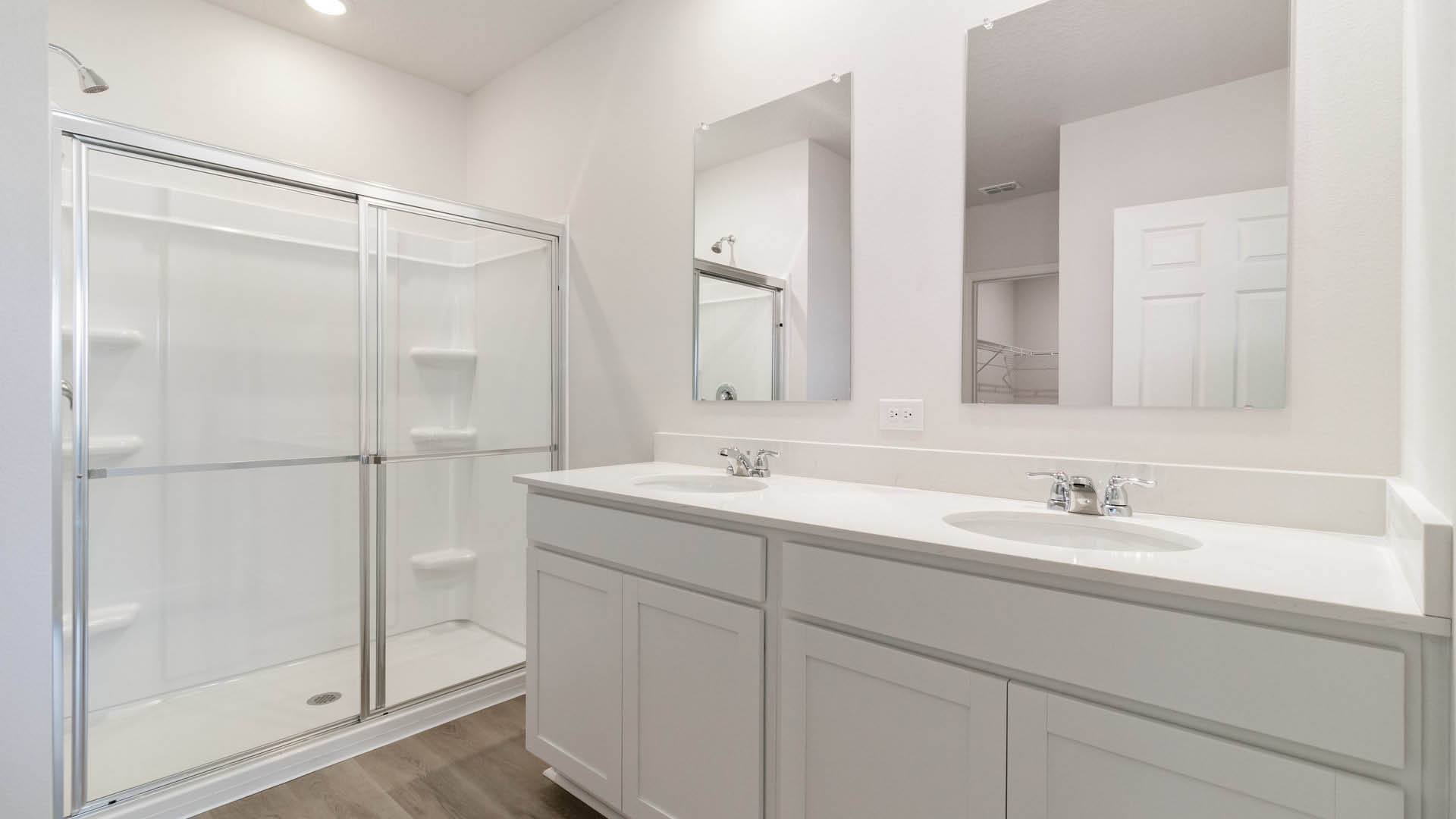 Spacious modern bathroom featuring a glass shower, double sink vanity, and neutral tile flooring with bright lighting.