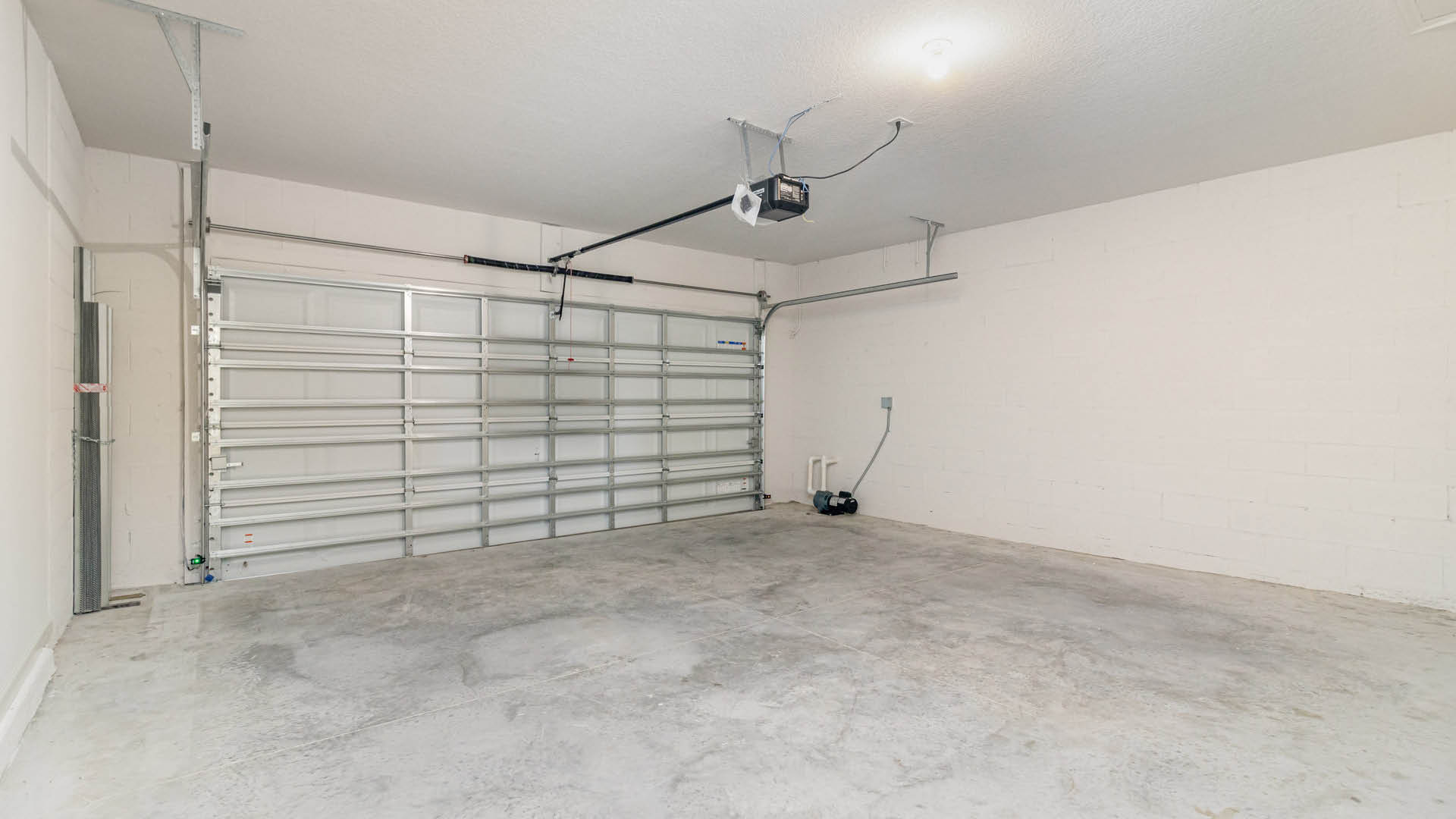 Spacious, two-car garage with concrete flooring, a garage door, and electrical pane along a white cinder block wall.