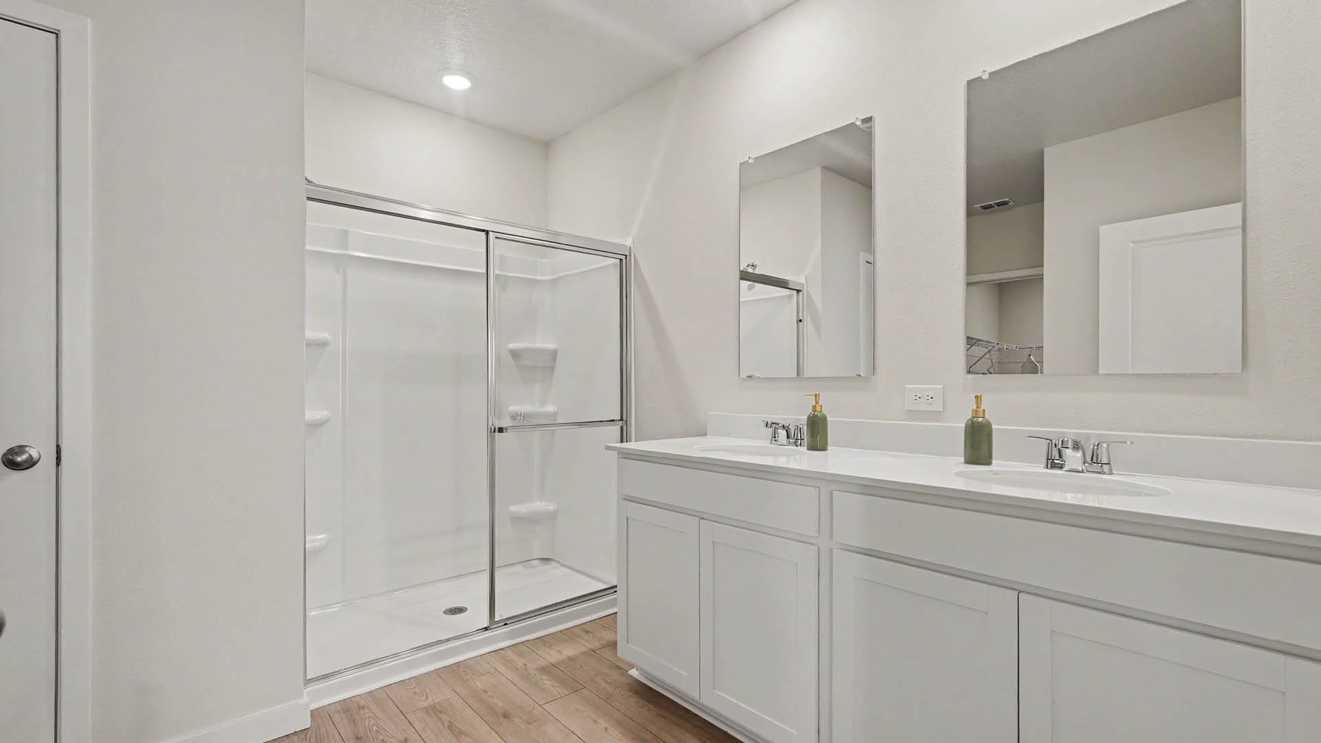 A modern bathroom features a glass-enclosed shower with sliding doors, a double sink vanity, and white cabinets.