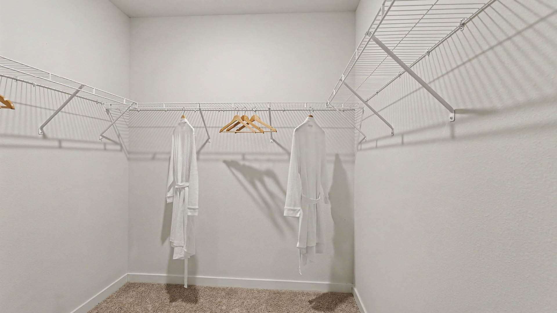 A spacious empty walk-in closet with white wire shelving and two white robes hanging on wooden hangers.
