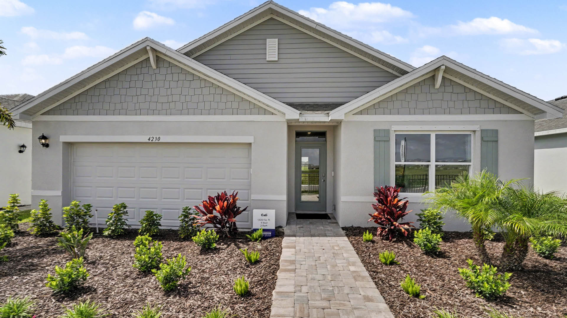 A modern single-story house with a two-car garage, a paved walkway, and landscaped front yard with small plants and shrubs.