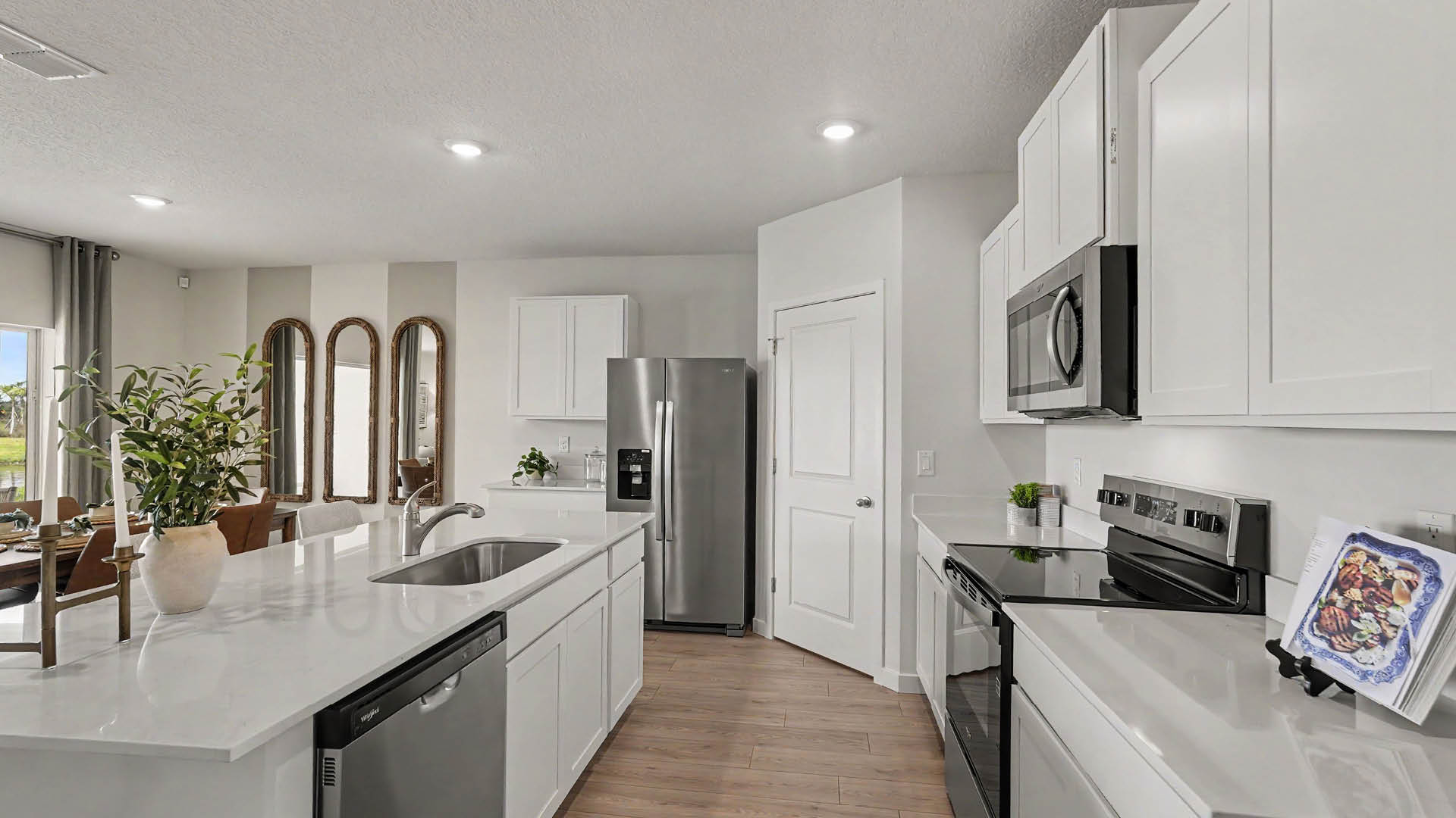 A modern kitchen with white cabinets, stainless steel appliances, a large island with a sink, and a potted plant on the countertop.