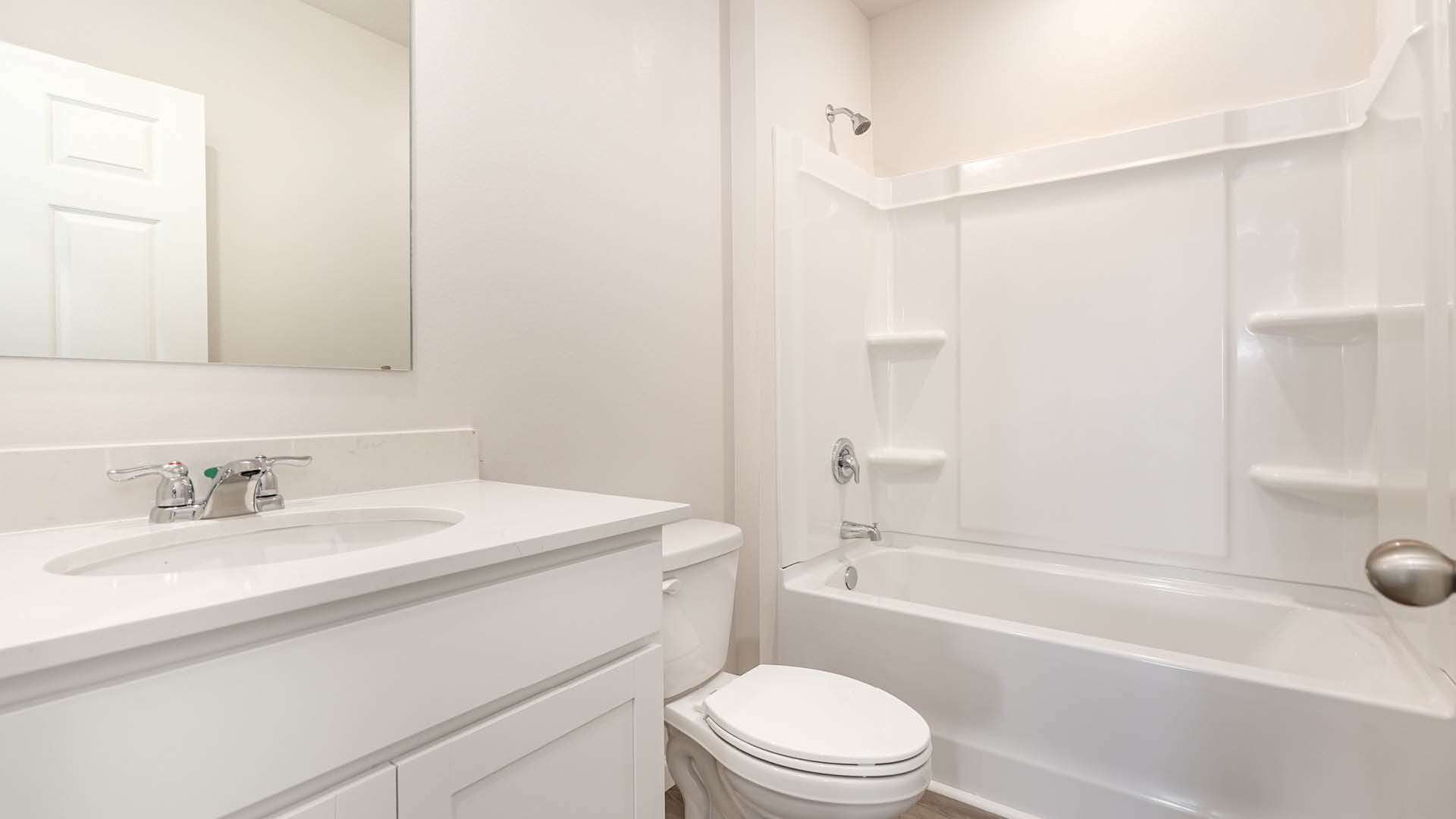 A clean, modern bathroom featuring quartz countertops, a bathtub with a shower, and a large mirror against neutral-colored walls.
