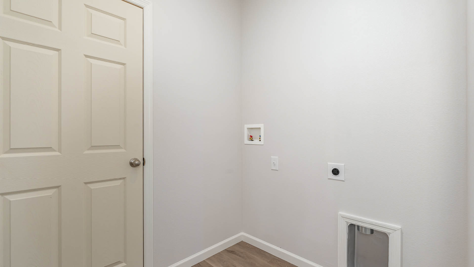 A laundry room with utility connections on the wall and Mohawk® Revwood Select Plank Flooring.