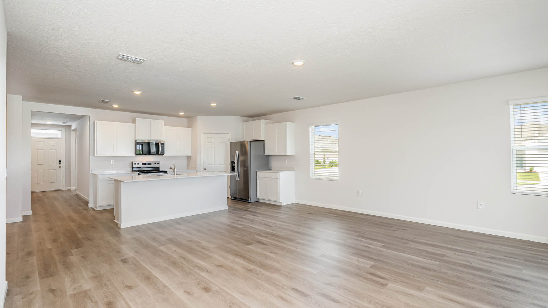 A spacious room, with a dining and kitchen area and Mohawk® Revwood Select Plank Flooring throughout.  An entryway hallway leading to the front door is visible.