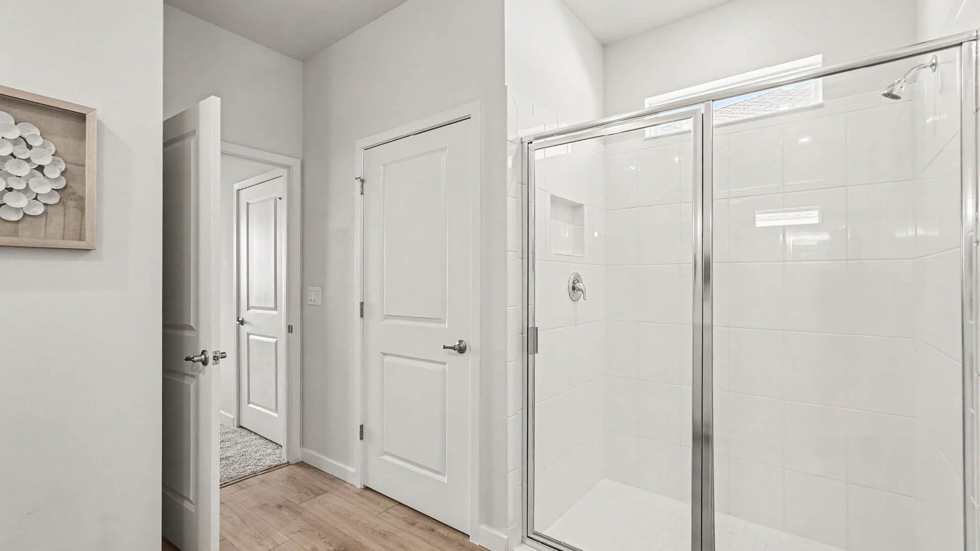 A modern bathroom features a glass-enclosed shower with white tile walls, two closed white doors, and Mohawk ® Revwood Select Plank Flooring.