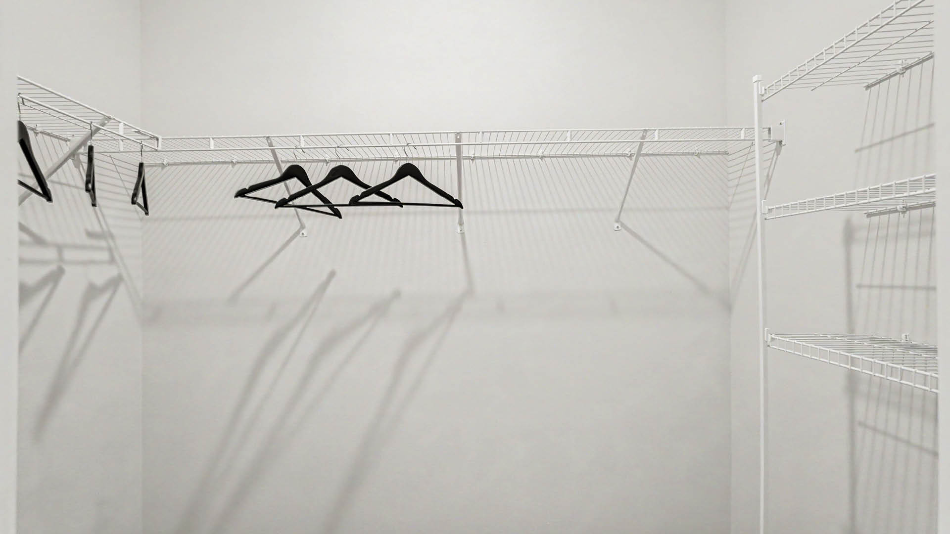 A large walk-in closet with several black hangers hanging on white wire shelves and racks.