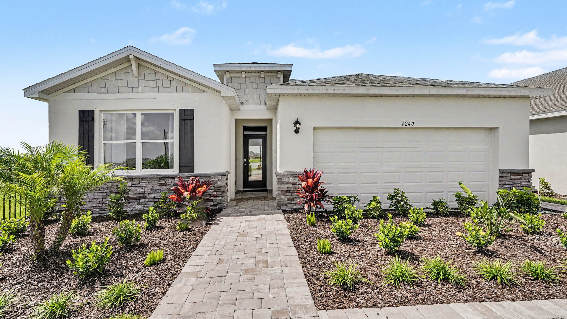 A modern single-story house with a light-colored exterior, stone accents, a two-car garage, and a landscaped front yard with a paved walkway leading to the entrance.