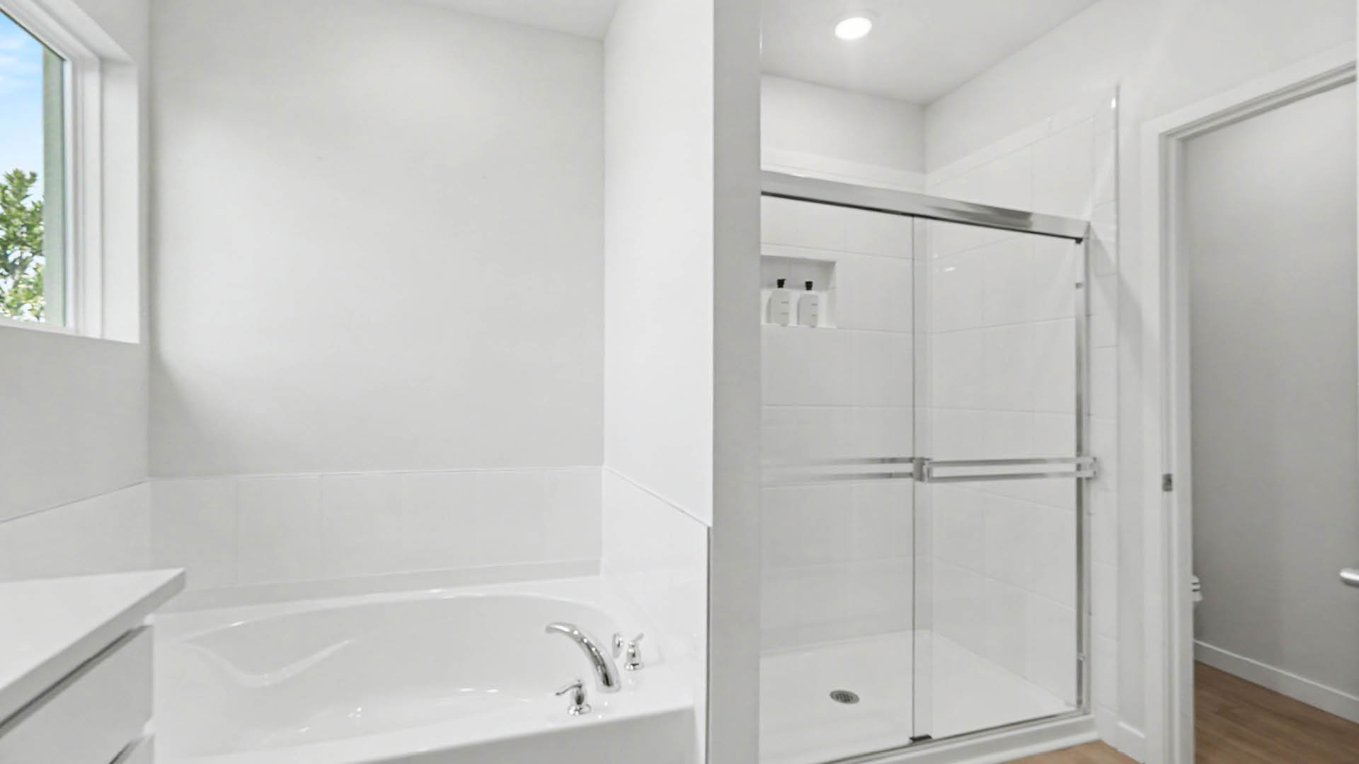A modern bathroom features a white bathtub next to a glass-enclosed shower and a small window letting in natural light.