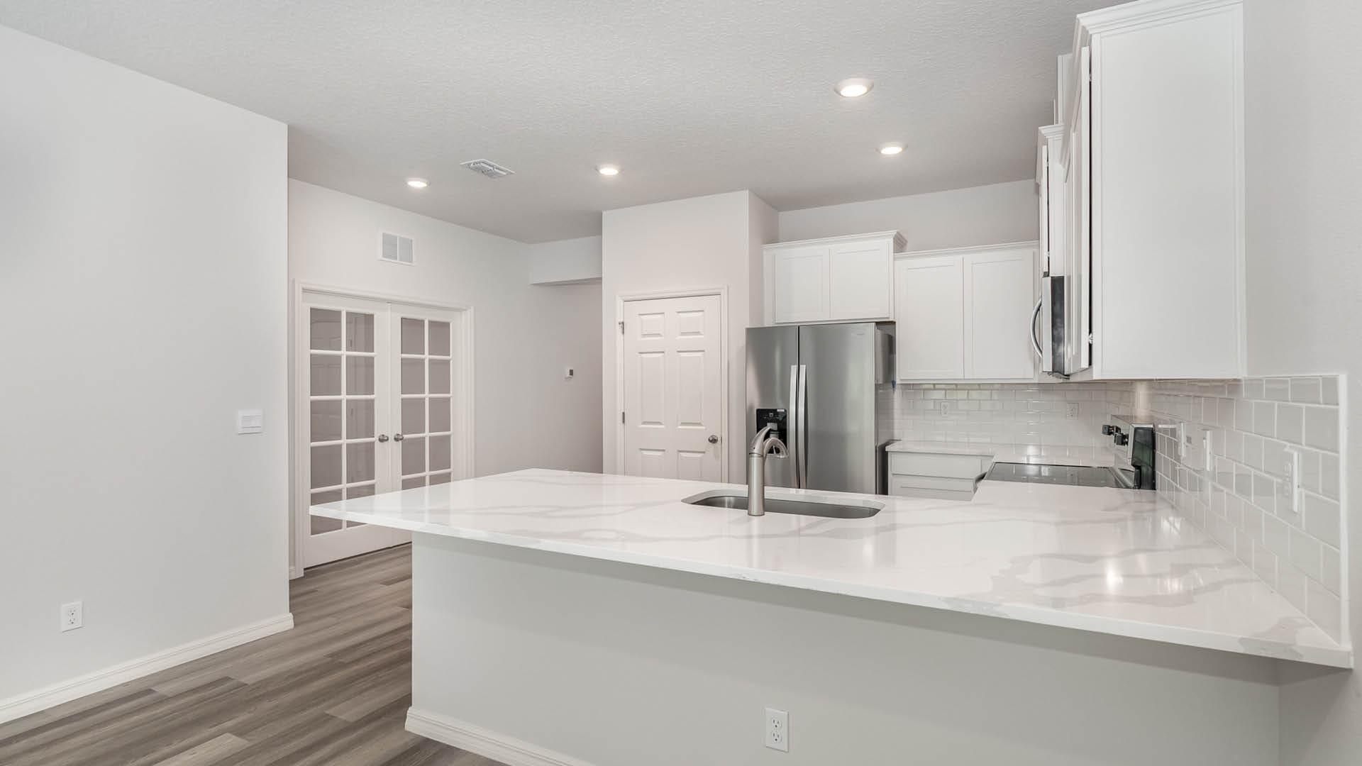 A modern kitchen with white cabinetry, stainless steel appliances, and a large countertop. A set of French doors is visible.