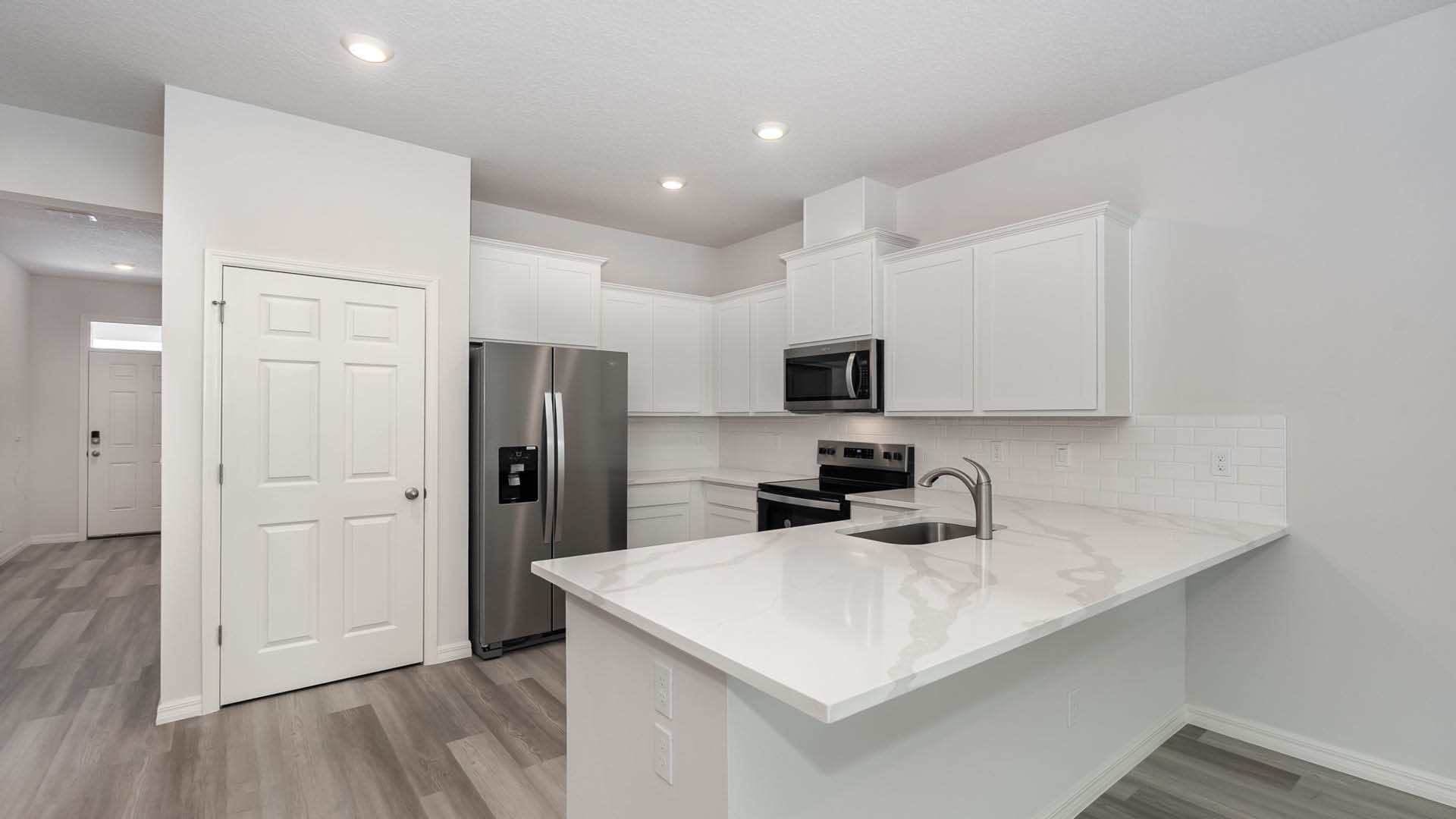 A modern kitchen with white cabinetry, stainless steel appliances, and a large countertop. Bright and welcoming entryway visible.