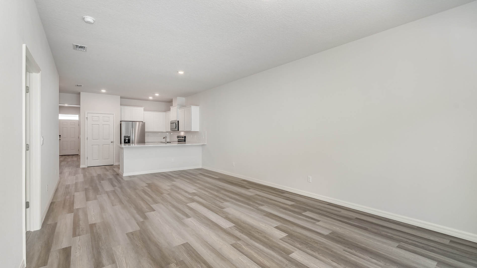 A bright, empty living and dining area with a view of a kitchen area.