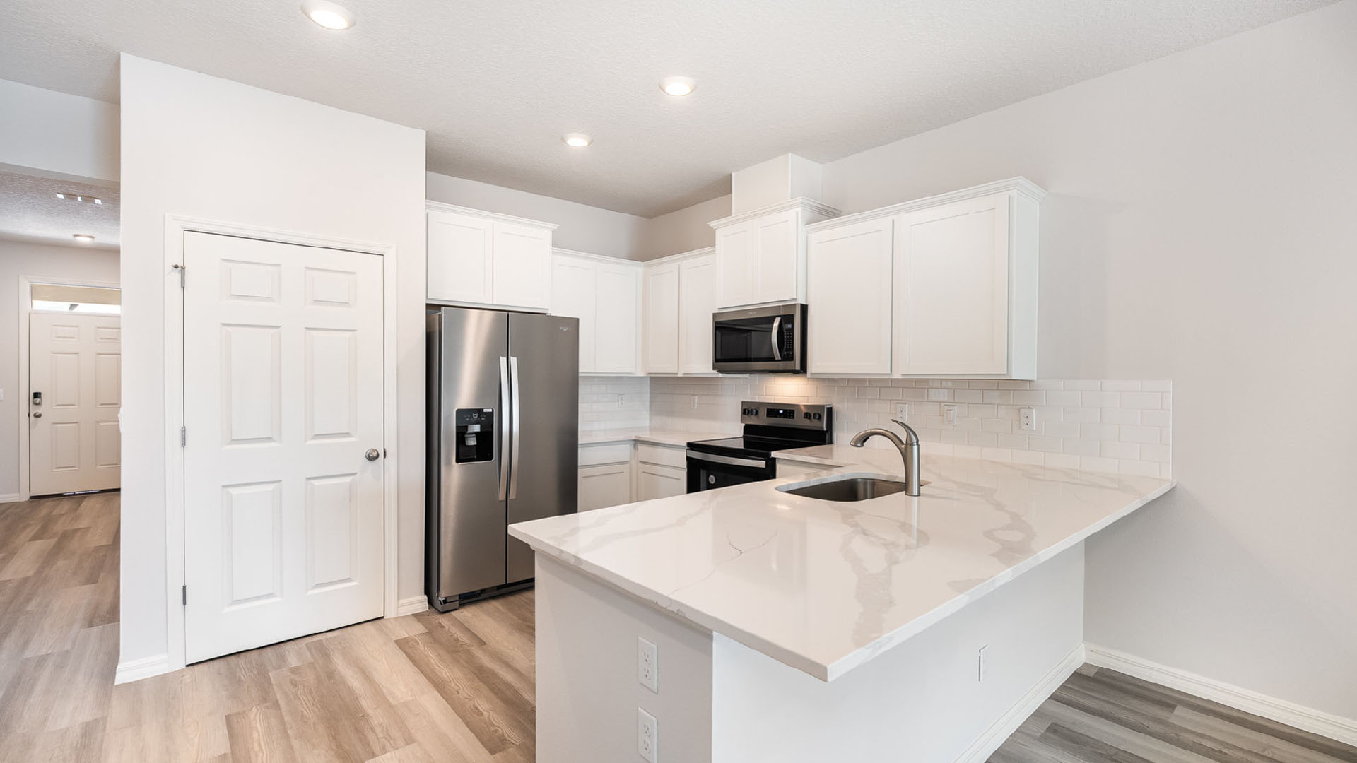 A modern kitchen with white cabinetry, stainless steel appliances, and a large countertop. Bright and welcoming entryway visible.