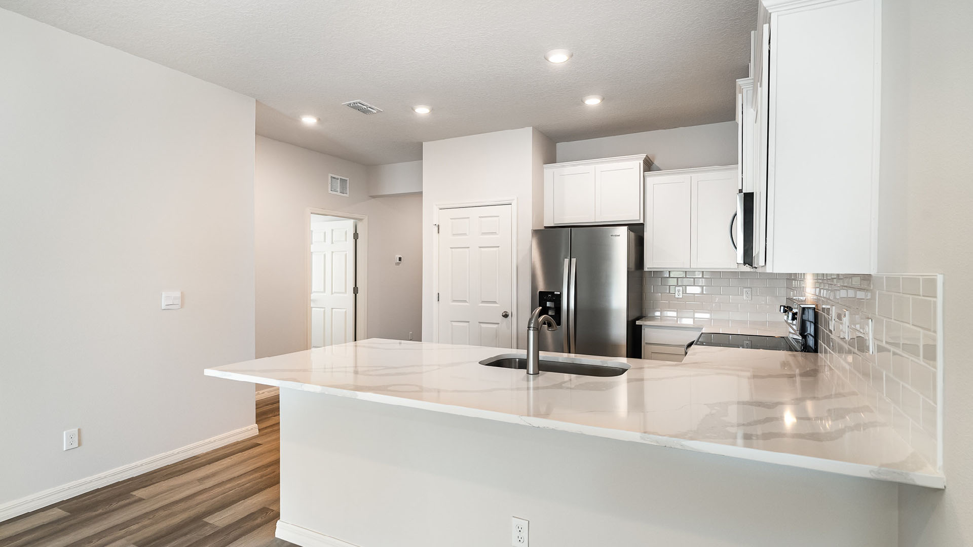 A modern kitchen with white cabinetry, stainless steel appliances, and a large countertop. An open door leading elsewhere is visible.