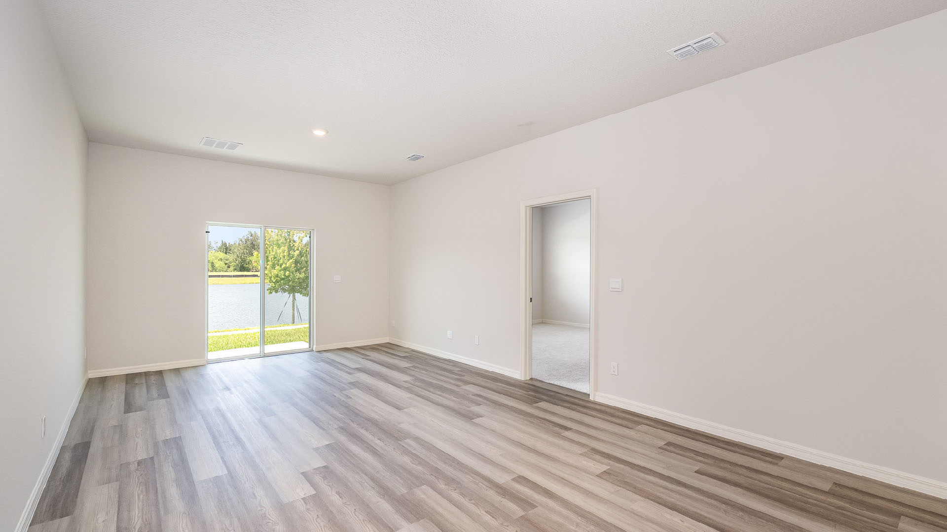 A bright, empty living and dining area featuring sliding glass doors leading to a covered outdoor patio. An open door leading to a bedroom is visible.