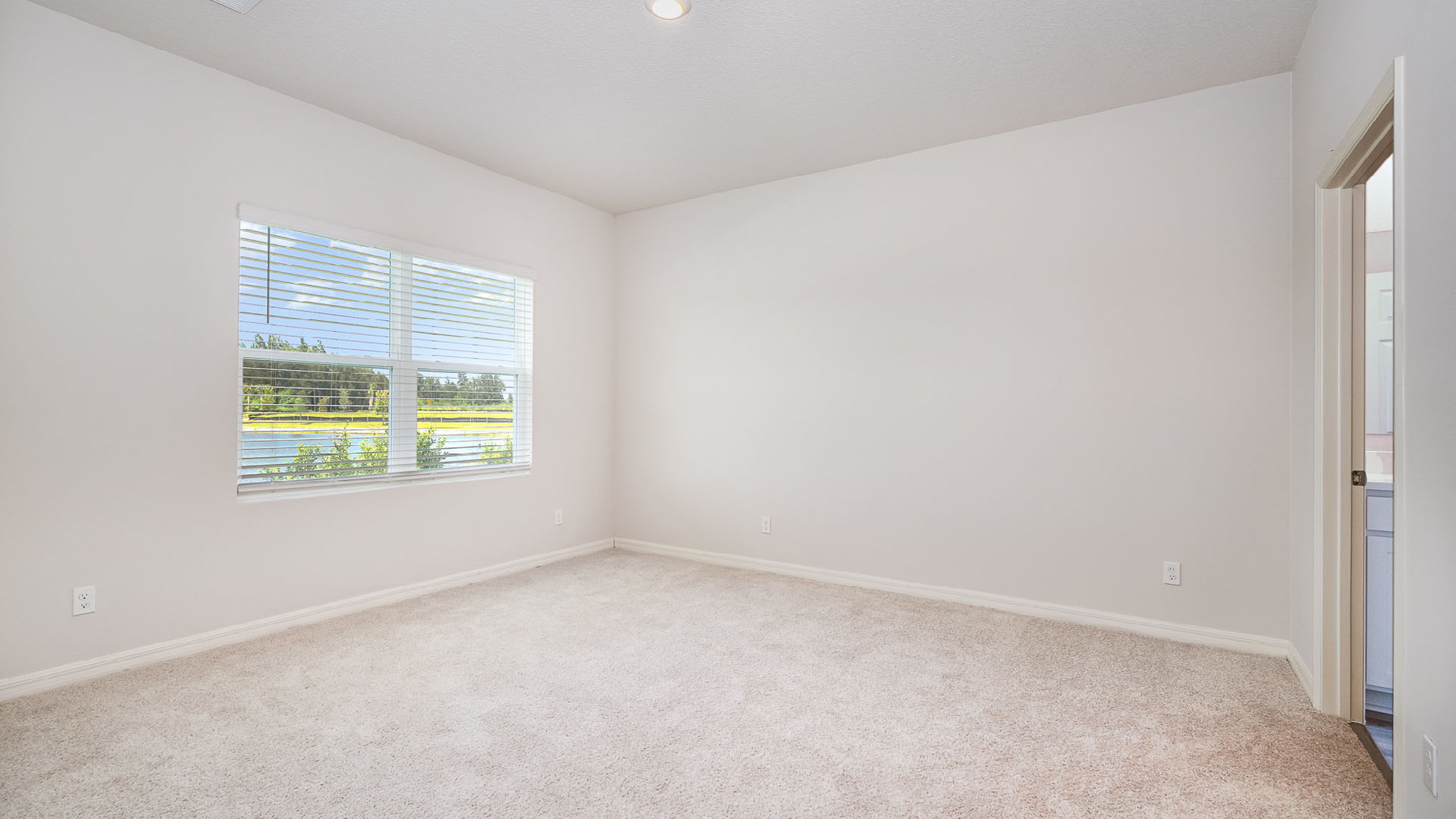 9.	A large bedroom with a large window. An open door leading to an ensuite bathroom is visible.