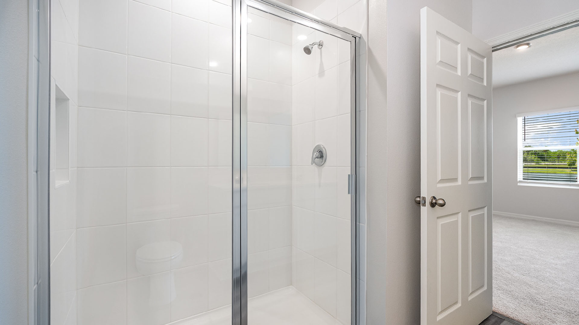 A spacious, modern bathroom featuring a walk-in shower. The open door to the bedroom is visible.