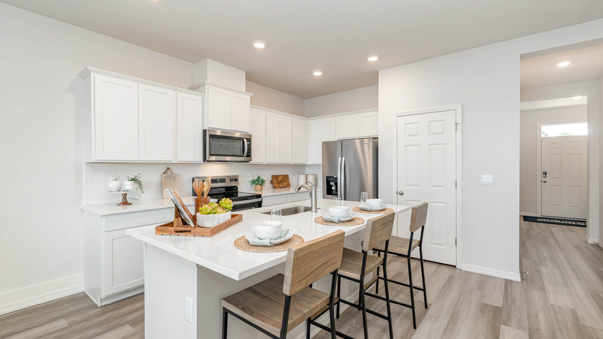 Modern kitchen featuring white cabinetry, stainless steel appliances, a large island with seating, and natural light from the entrance.