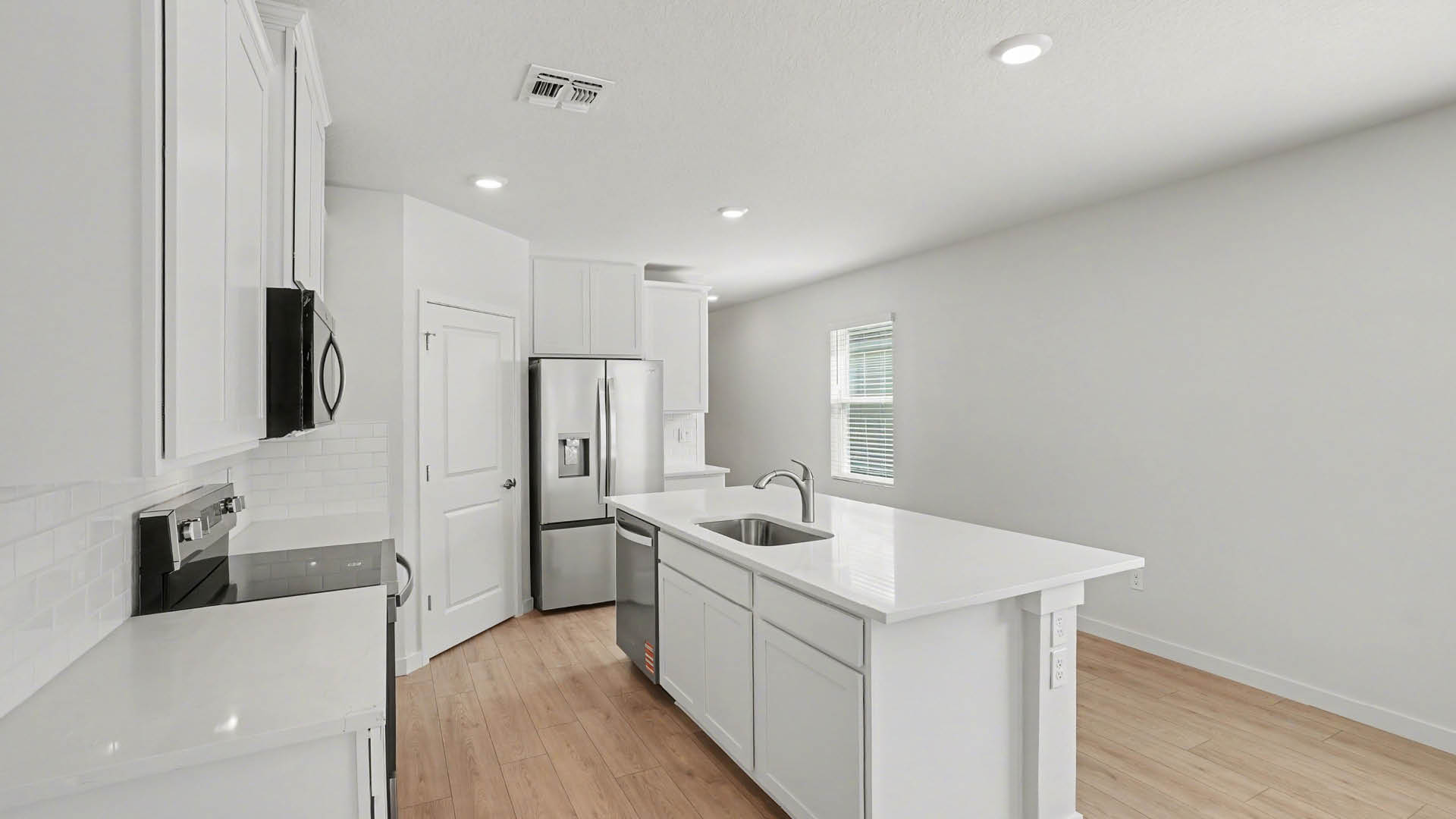 A modern kitchen with white cabinetry, quartz countertops, stainless steel appliances, and a large island with plenty of room for seating.