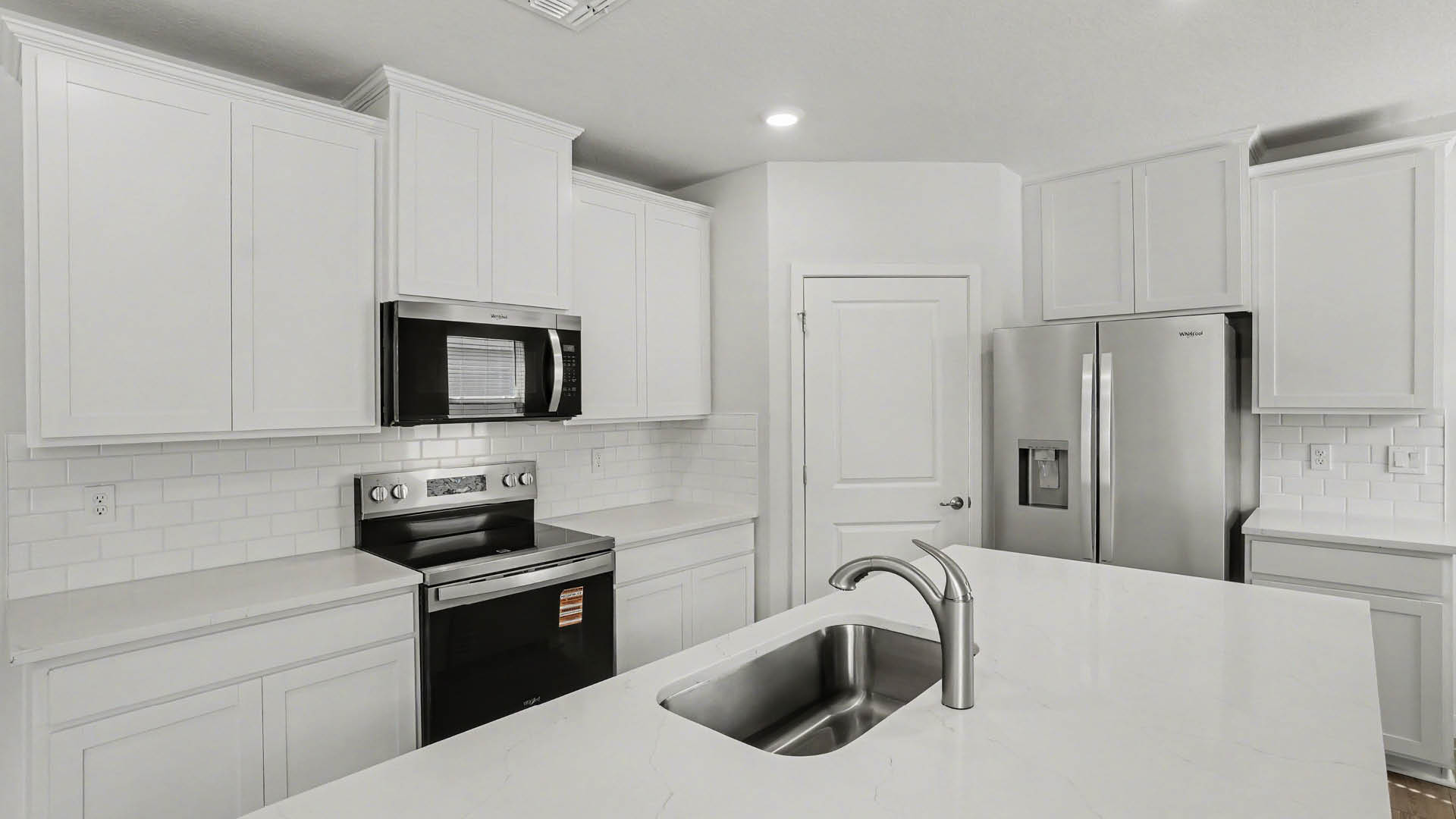 A modern kitchen with white cabinetry, quartz countertops, stainless steel appliances and a closed pantry door.