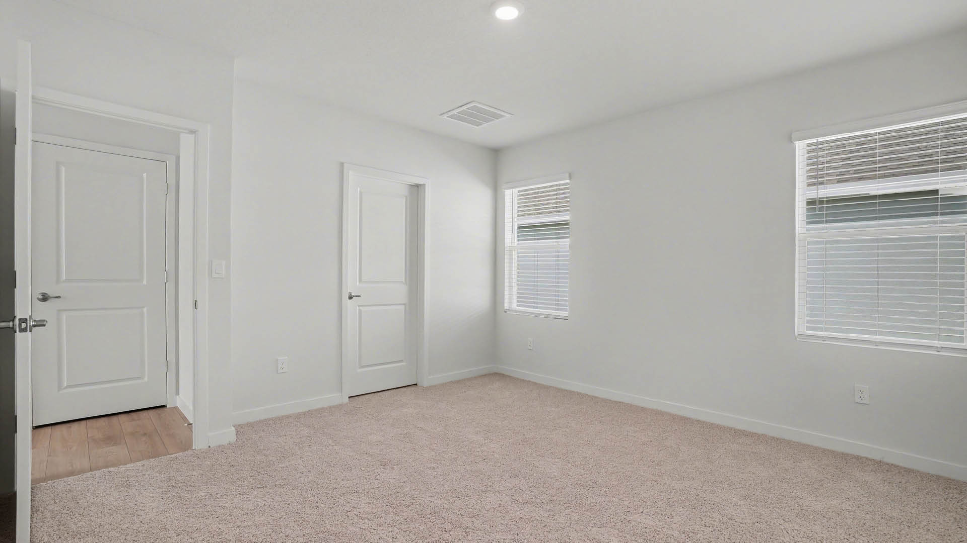 A large bedroom with beige carpet and two windows. An open door leading out of the room and a closed closet door are visible.