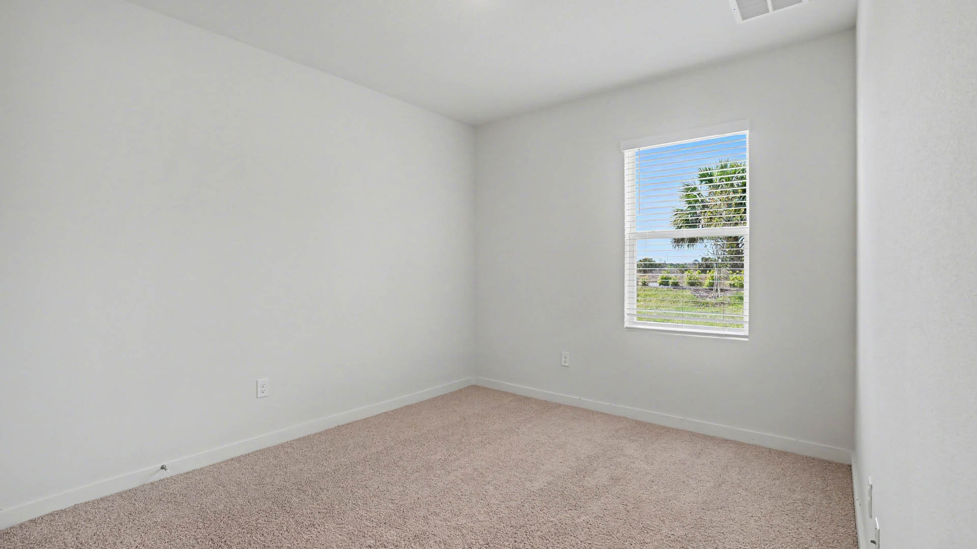 A large bedroom with beige carpet and white walls. An open door leading out of the room and a closed closet door are visible.