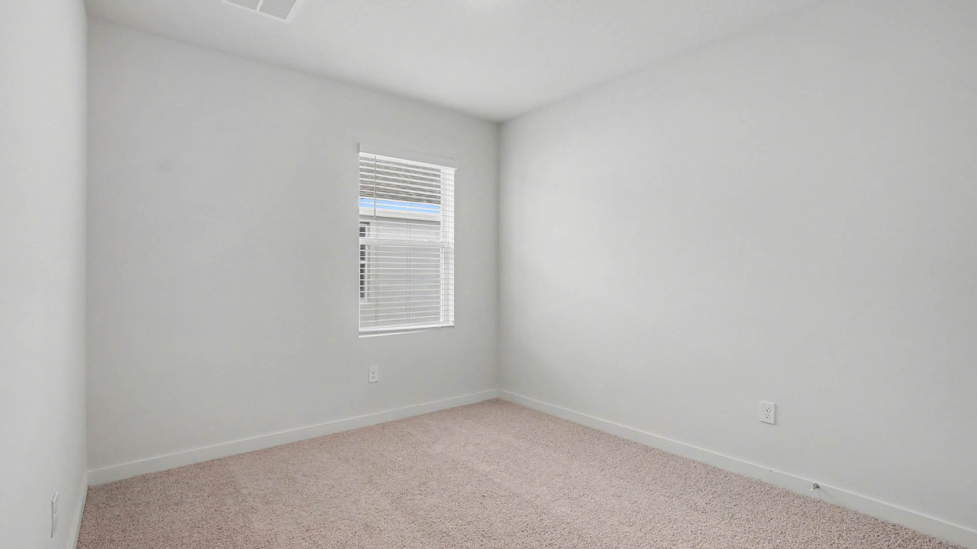 A large bedroom with beige carpet and white walls. An open door leading out of the room and a closed closet door are visible.