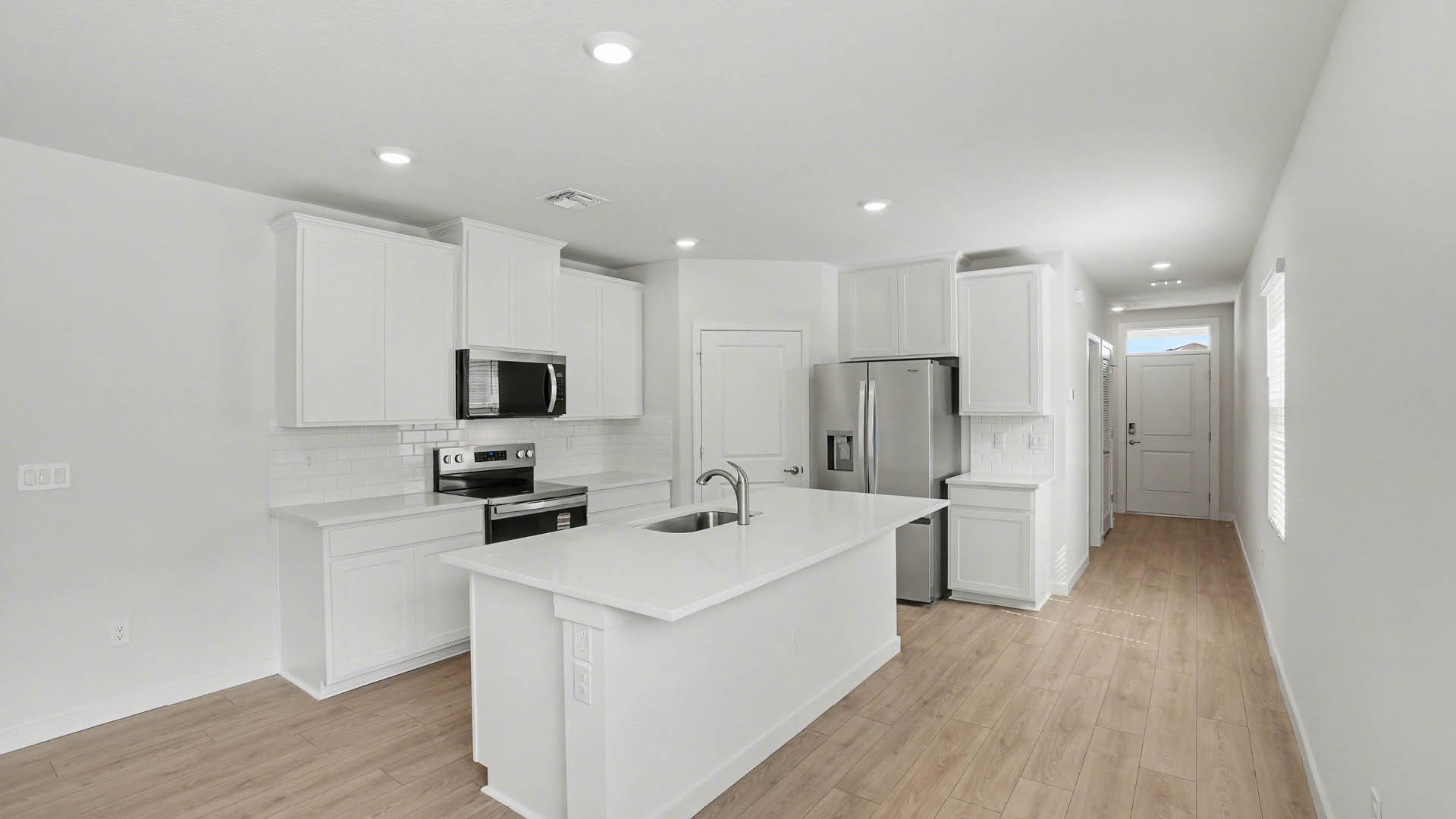 A modern kitchen with white cabinetry, quartz countertops, stainless steel appliances, and a large island. A bright and welcoming entryway is also visible.