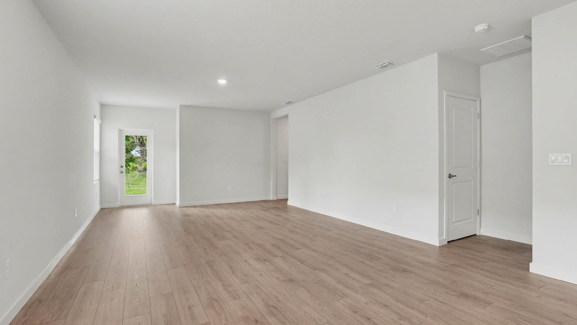 A spacious dining and living area with Mohawk® Revwood Select Plank Flooring throughout. There is a closed door leading to another area and the closed back door leading to a covered patio.