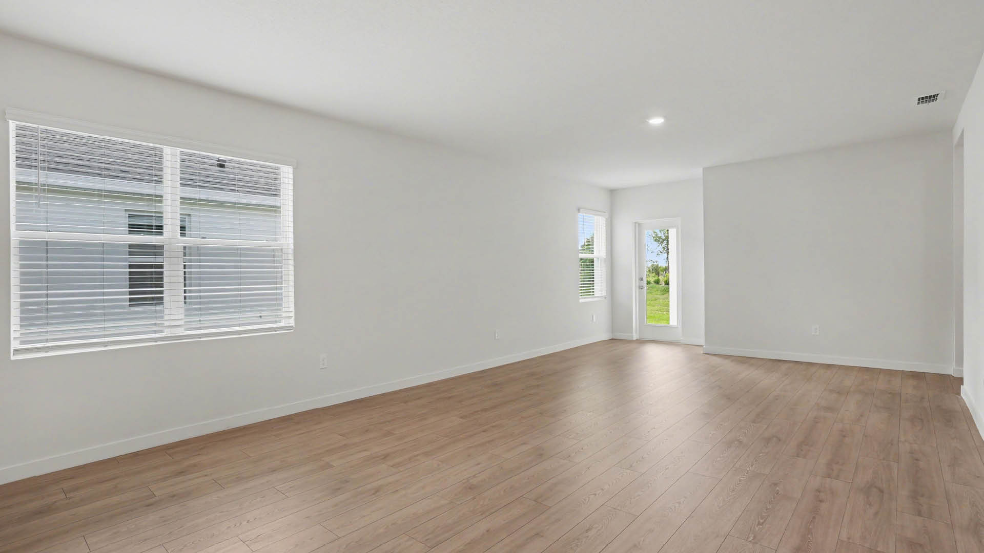 A spacious dining and living area with Mohawk® Revwood Select Plank Flooring throughout. There is a closed back door leading to a covered patio and several windows along the wall.