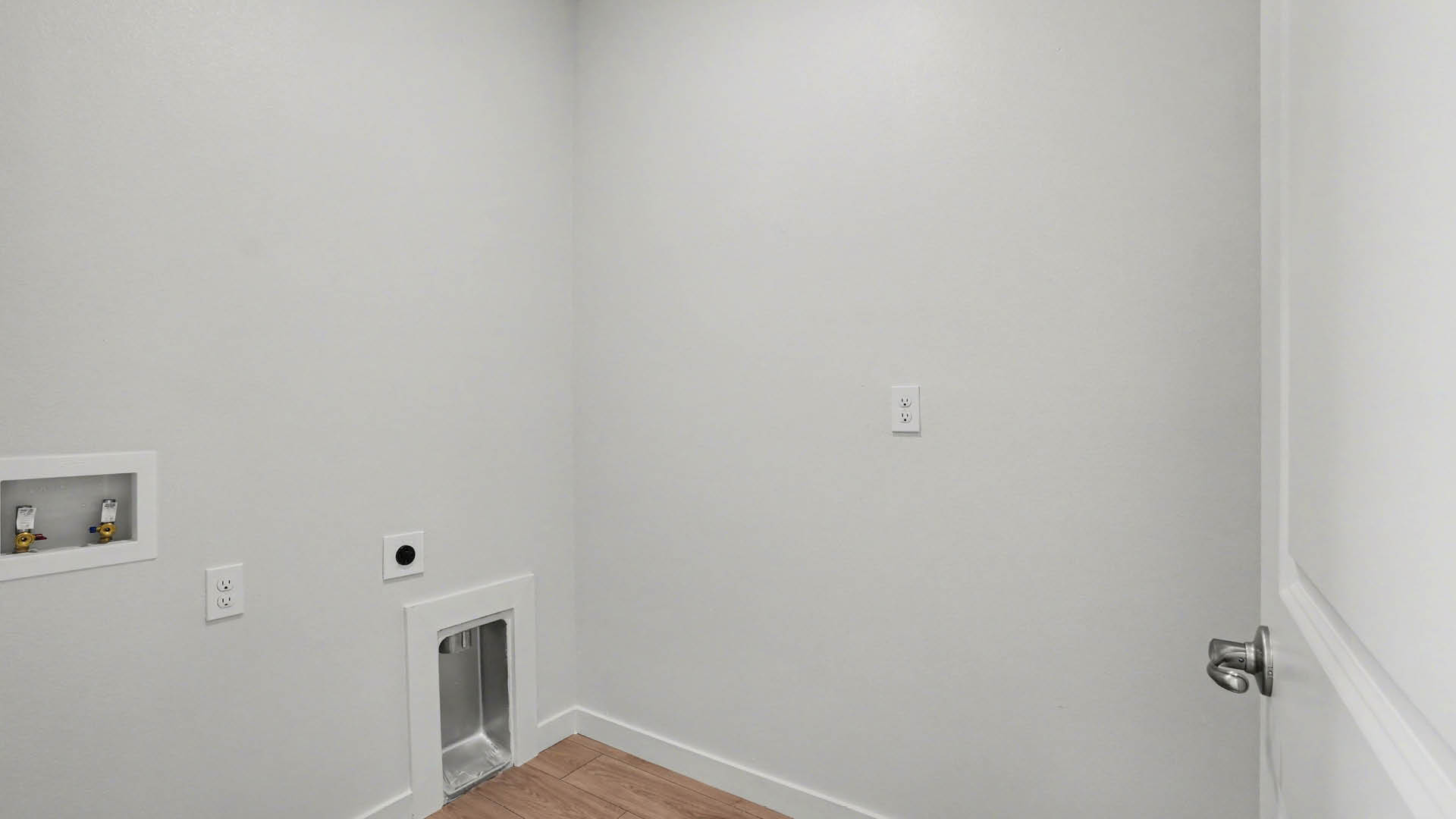 A laundry room with utility connections on the wall and Mohawk® Revwood Select Plank Flooring.