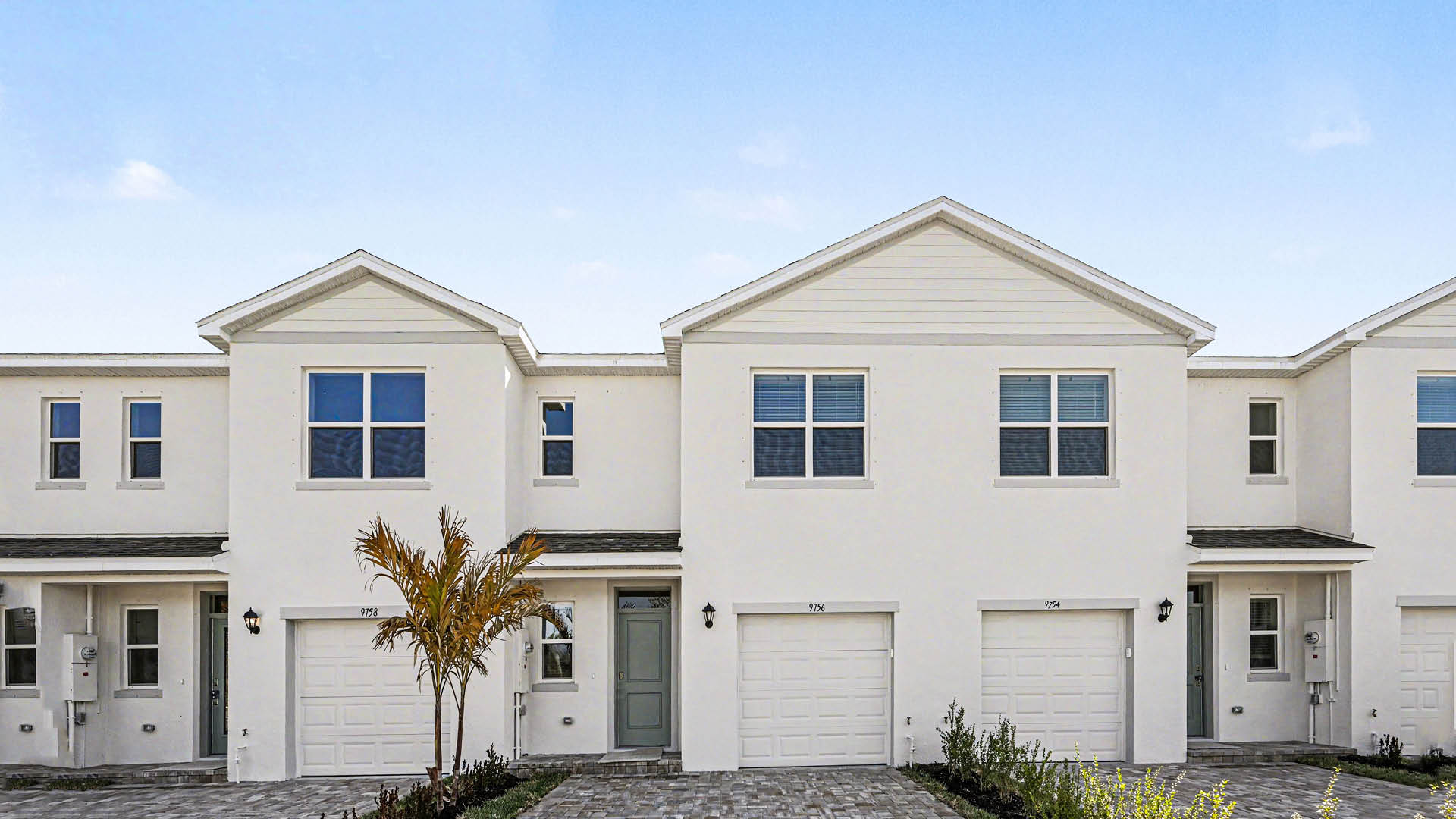 A row of  light townhomes with attached single-car garages and covered doorways.