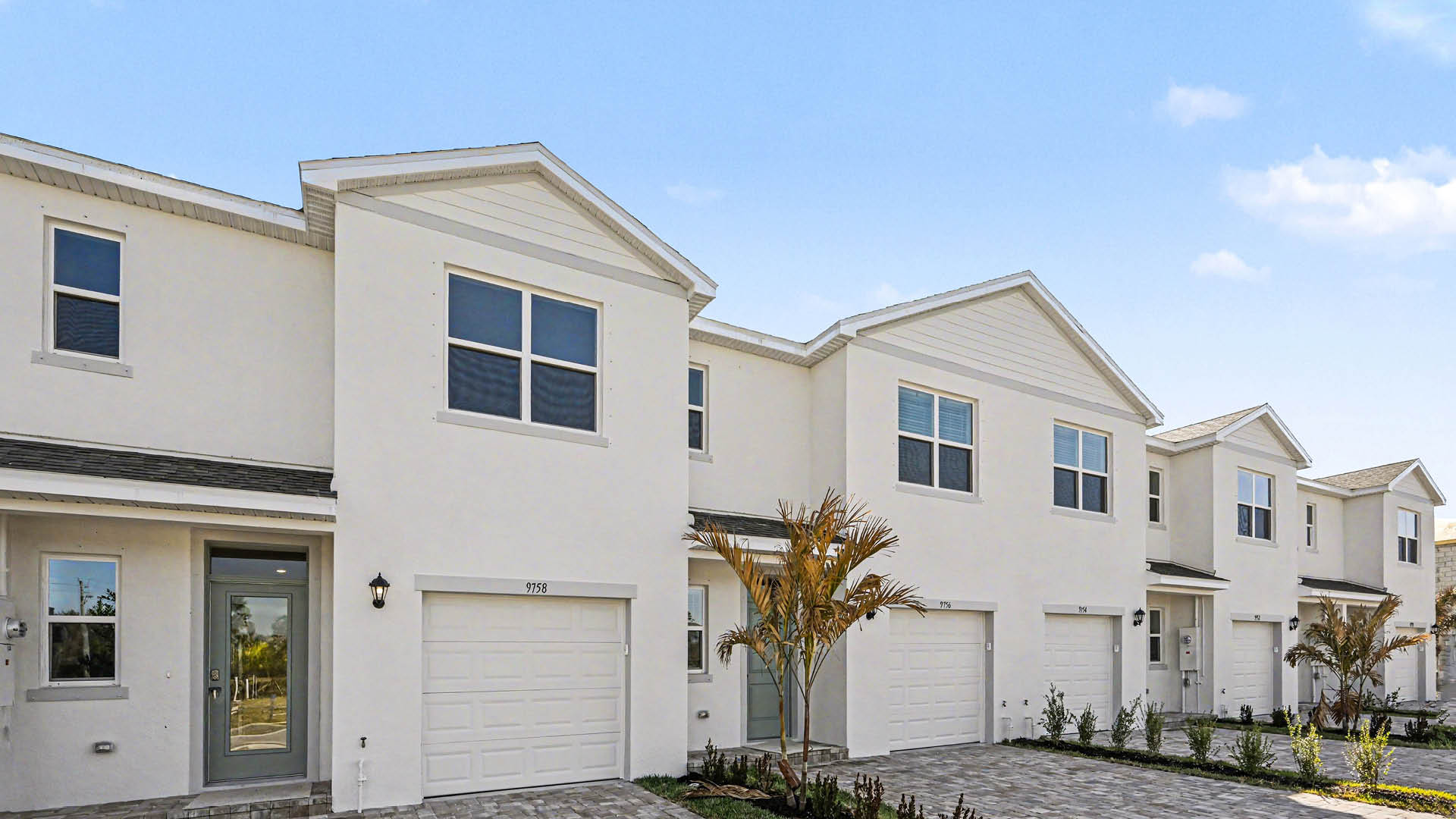 A row of  light townhomes with attached single-car garages and covered doorways.