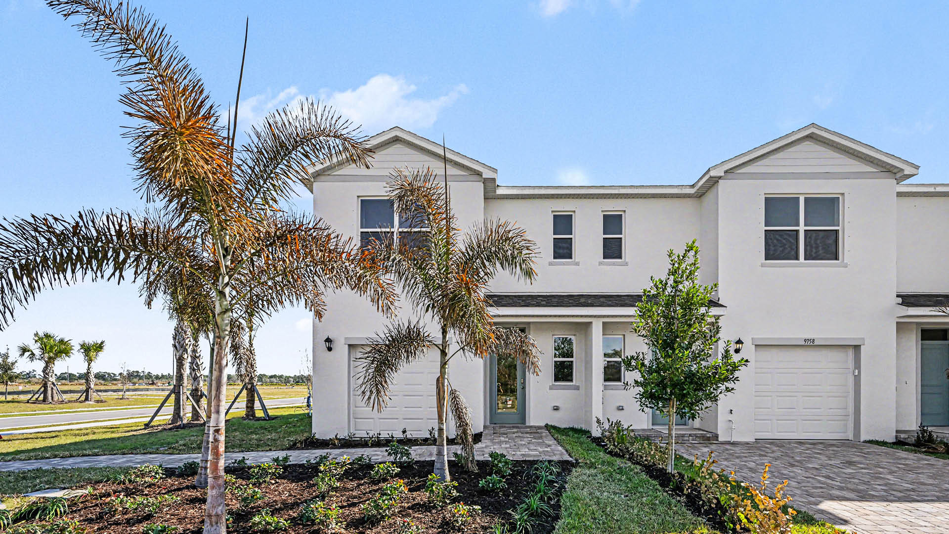A row of  light townhomes with attached single-car garages and covered doorways. The end unit is surrounded by landscaping.