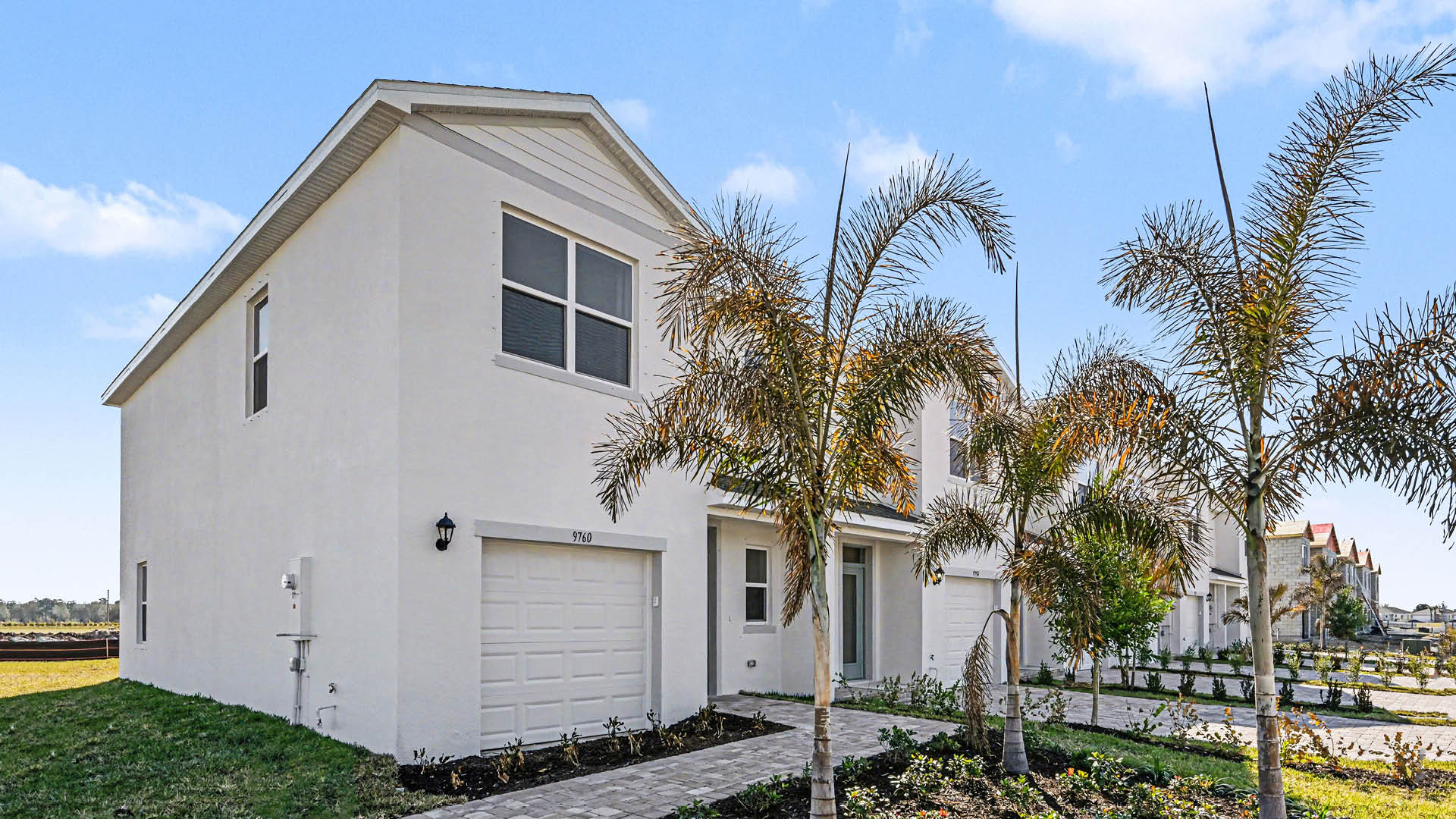 A row of  light townhomes with attached single-car garages and covered doorways. The end unit is surrounded by landscaping.
