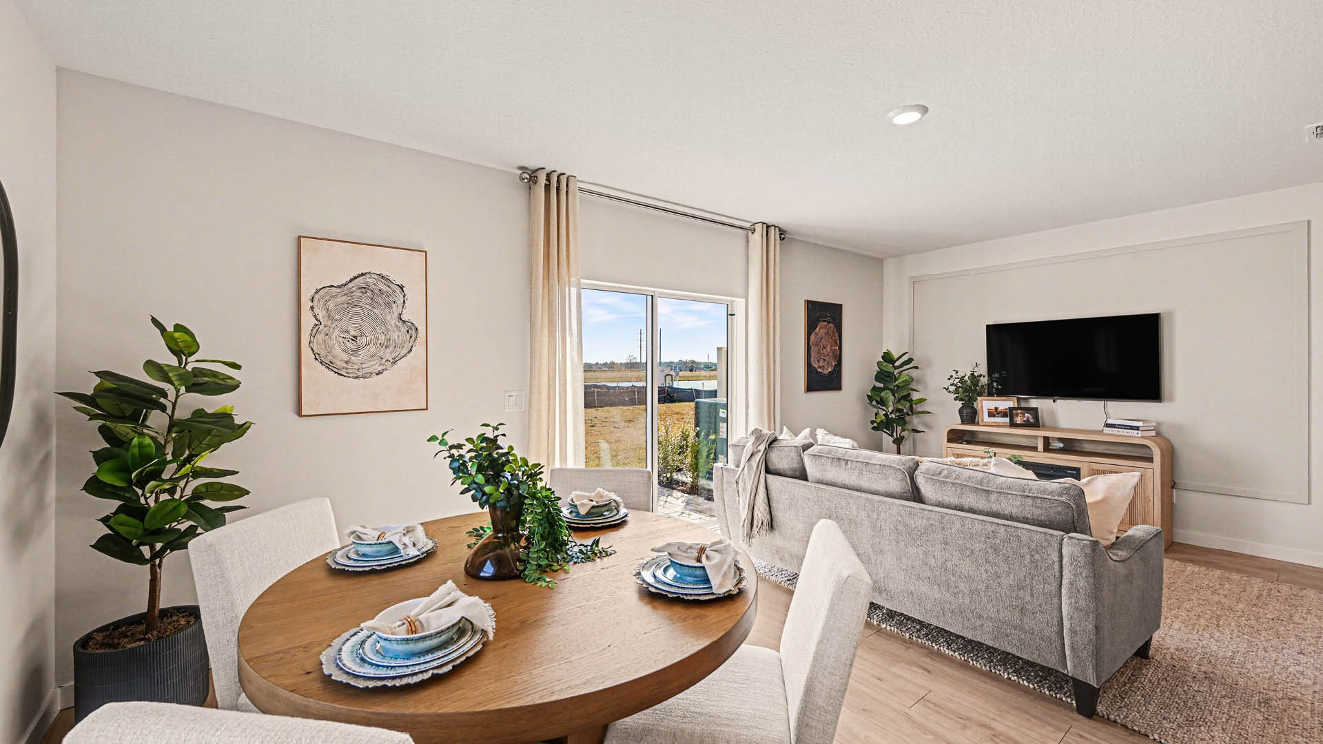 A bright dining area featuring sliding glass doors leading to a green outdoor area. The living room with Mohawk® Revwood Select Plank Flooring is visible.