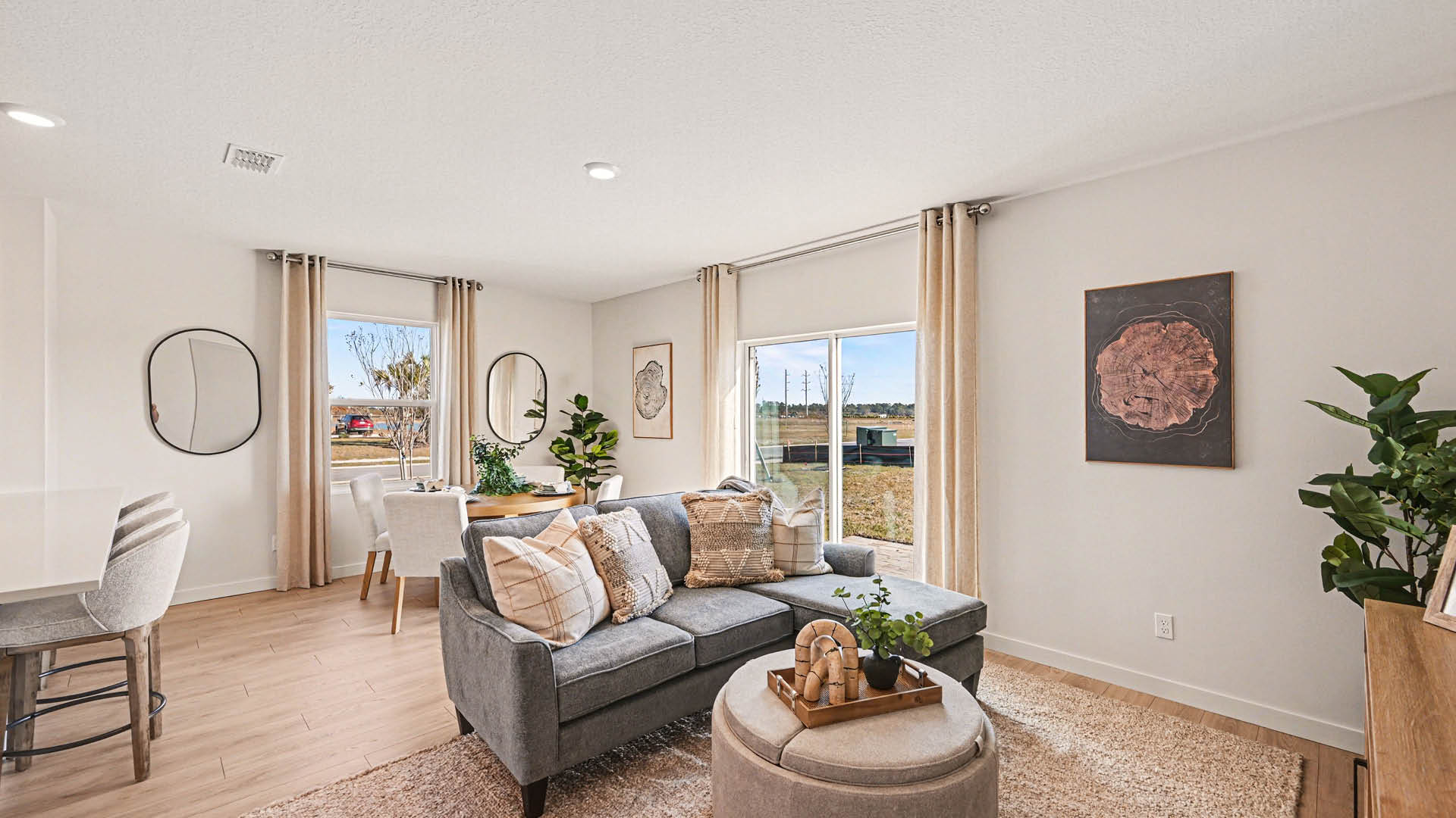 A living room with a dining area behind it. There is a large window, sliding glass doors to the backyard, and Mohawk® Revwood Select Plank Flooring throughout.