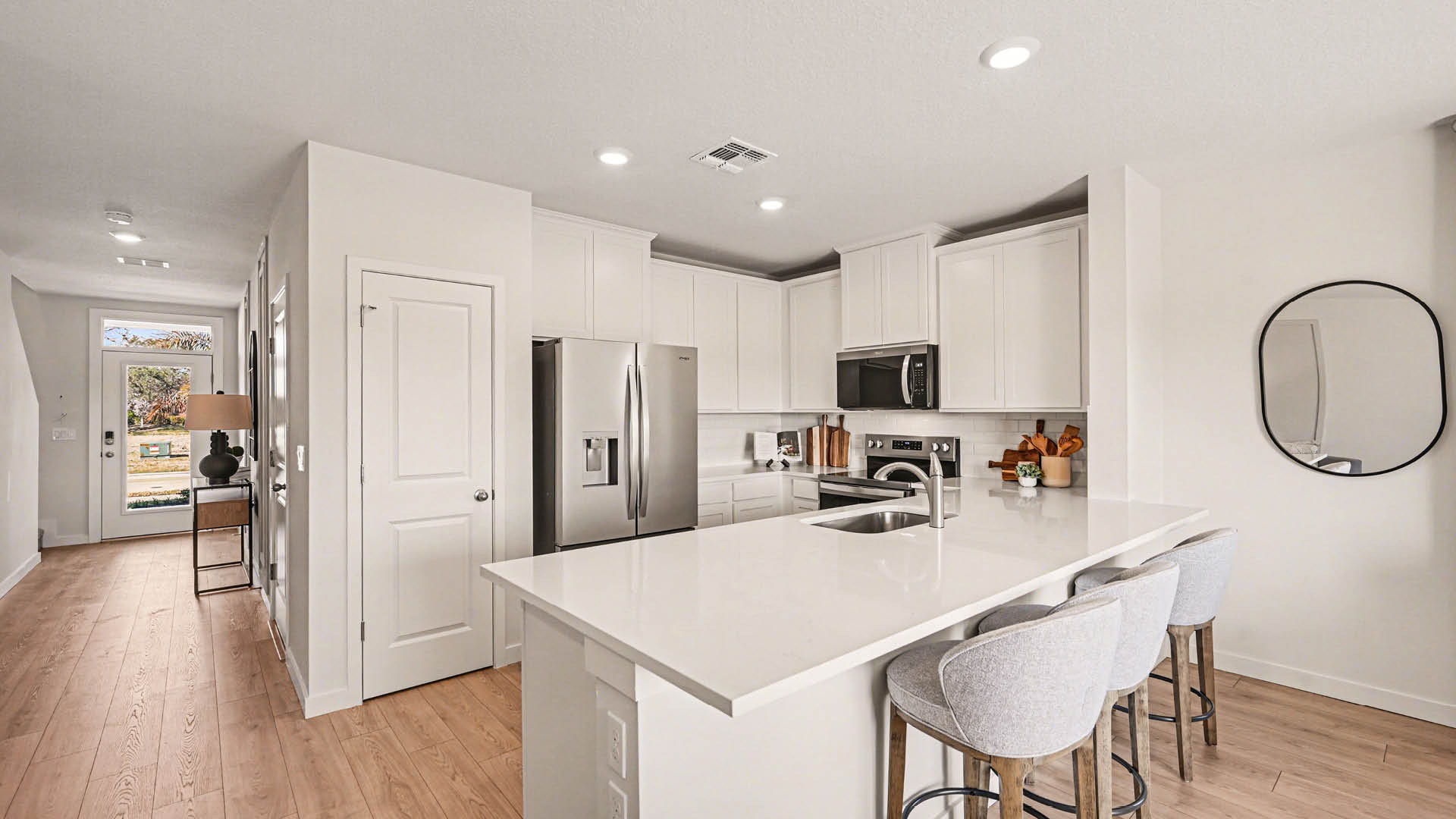 A large kitchen with quartz countertops, stainless steel appliances, and a peninsula with seating. An entryway hallway leading to the front door is visible.