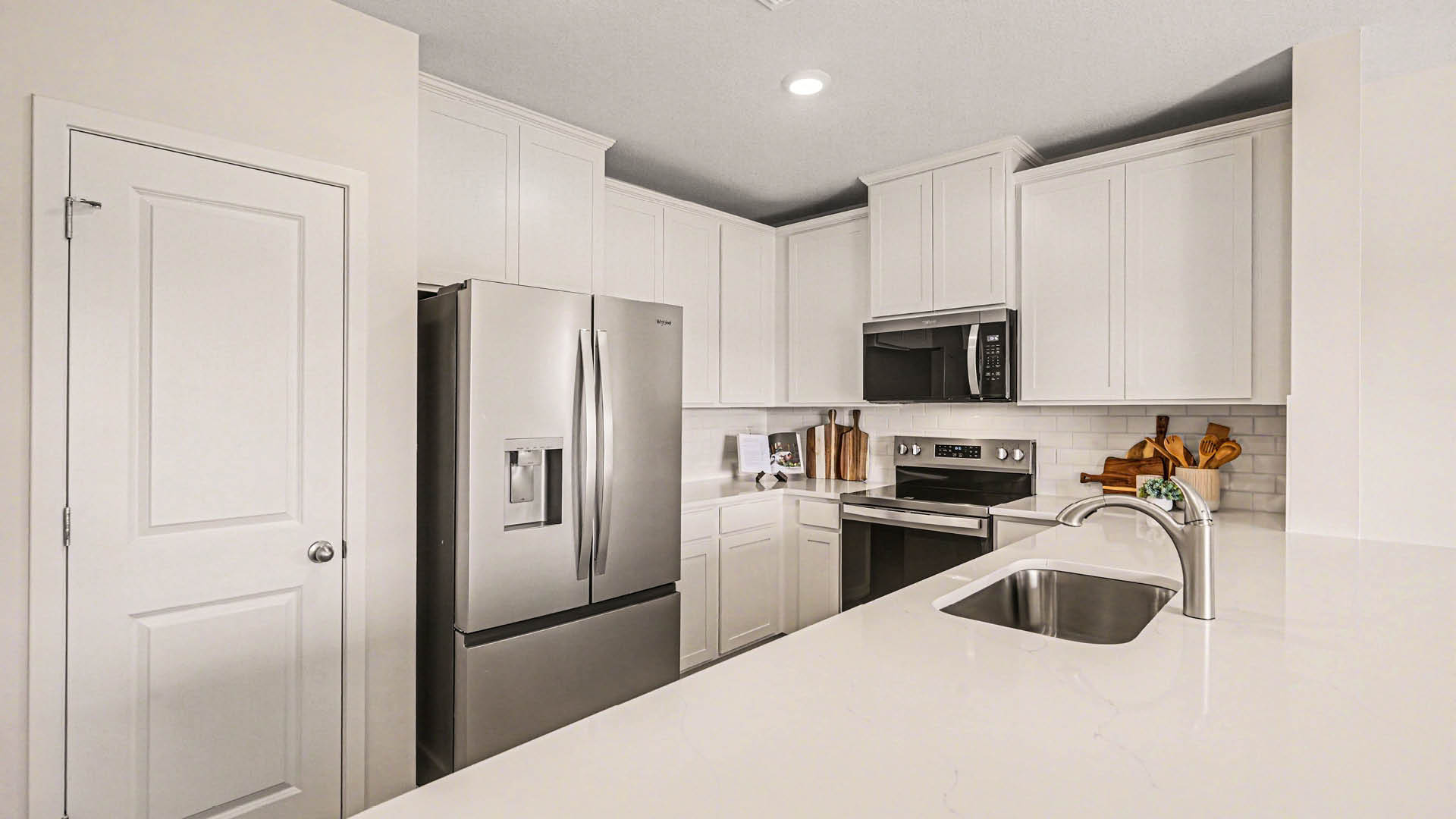 A large kitchen with quartz countertops, stainless steel appliances, and modern, white cabinetry. A kitchen pantry door is visible.