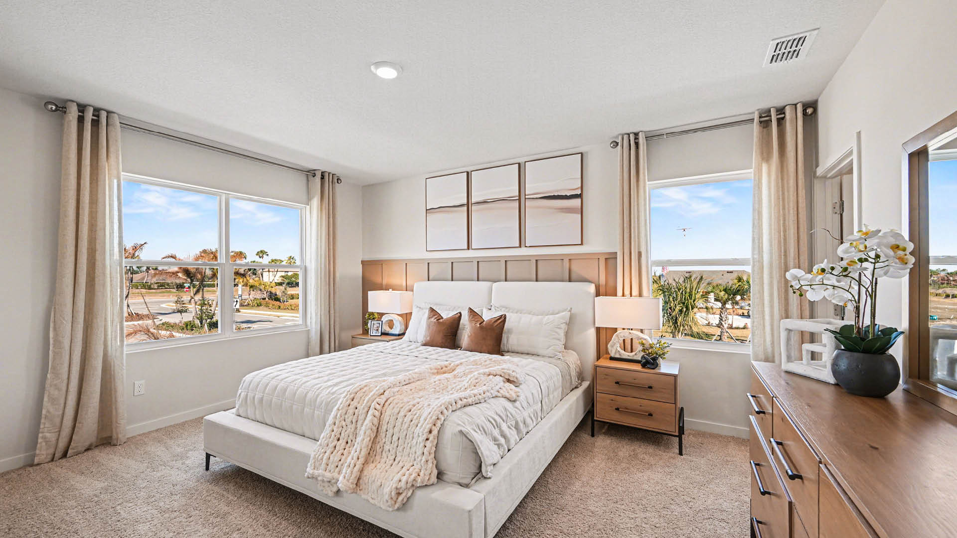 A large bedroom with beige carpet, white walls, and two windows, allowing natural light to illuminate the space.