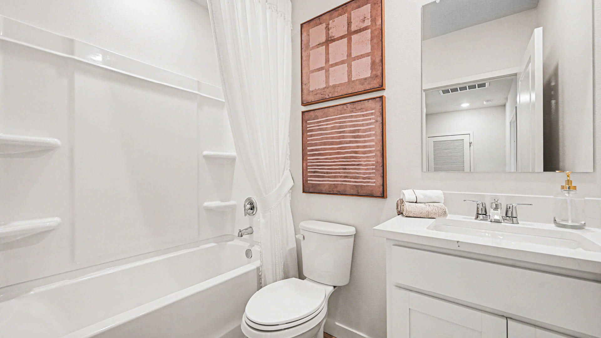 A clean, modern bathroom featuring quartz countertops, a bathtub with a shower, and a large mirror against neutral-colored walls.