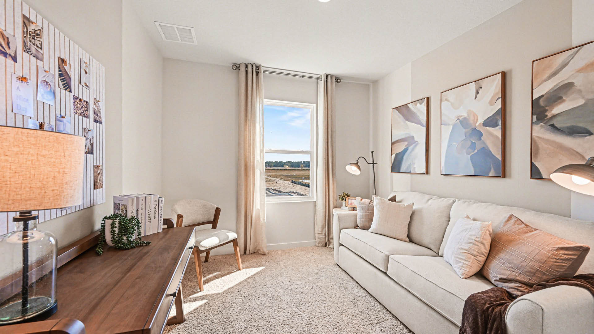 A multipurpose room furnished as a living room with a couch, chair, and table. A large window lets in natural light. Several paintings adorn the walls.