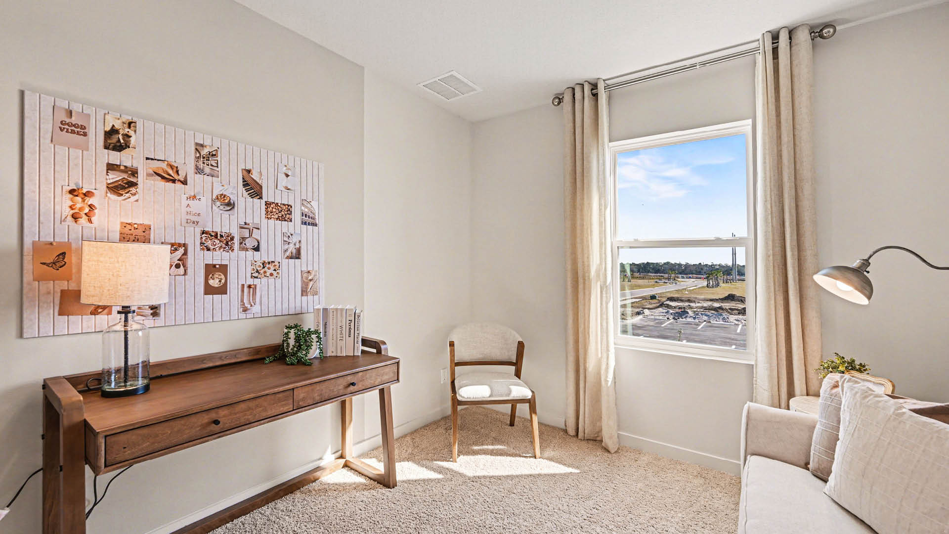 A multipurpose room furnished as a living room with a couch, chair, and table. A large window lets in natural light. Several paintings adorn the walls.