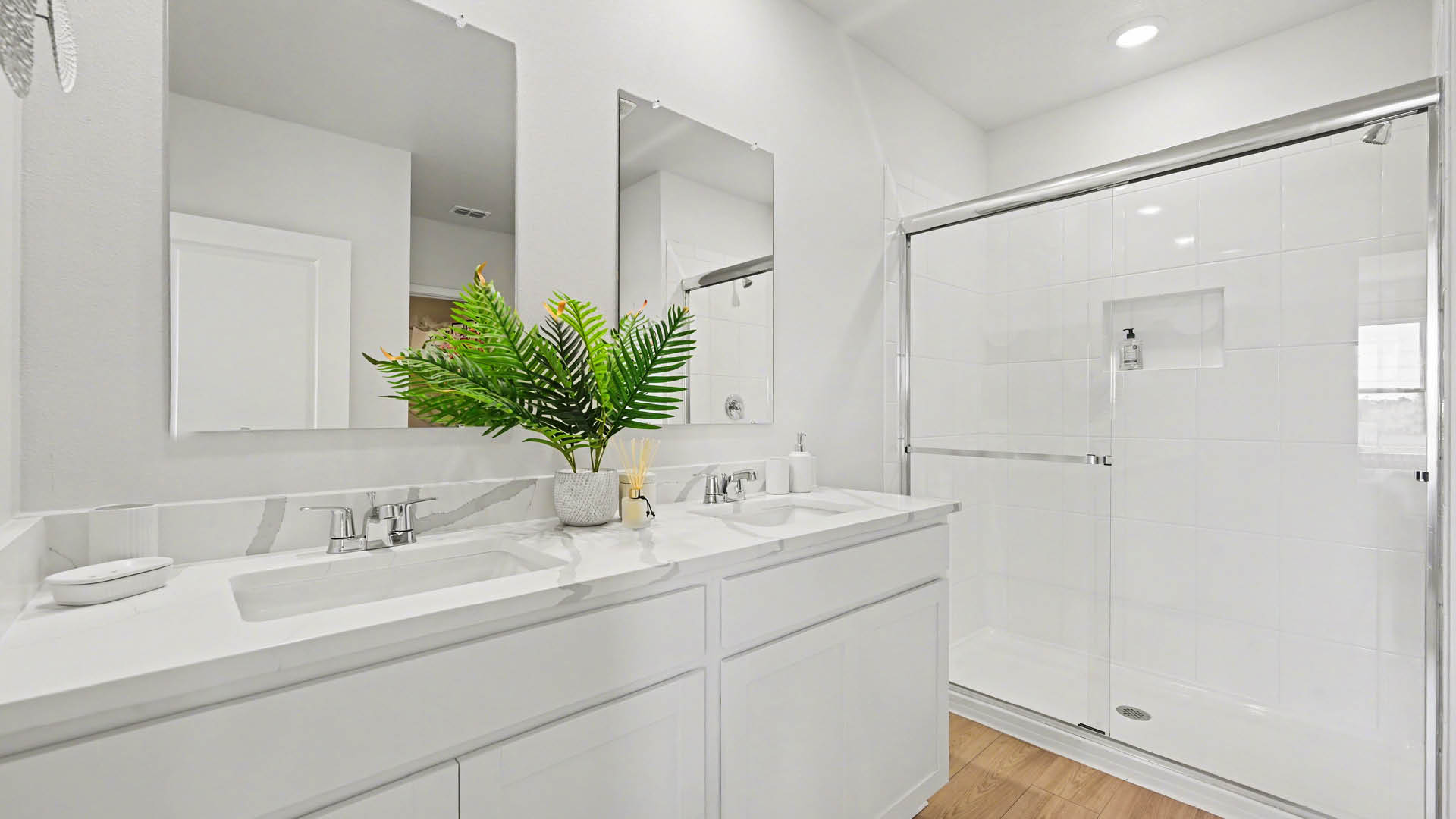 Spacious modern bathroom featuring a glass shower, double sink vanity, and bright lighting.
