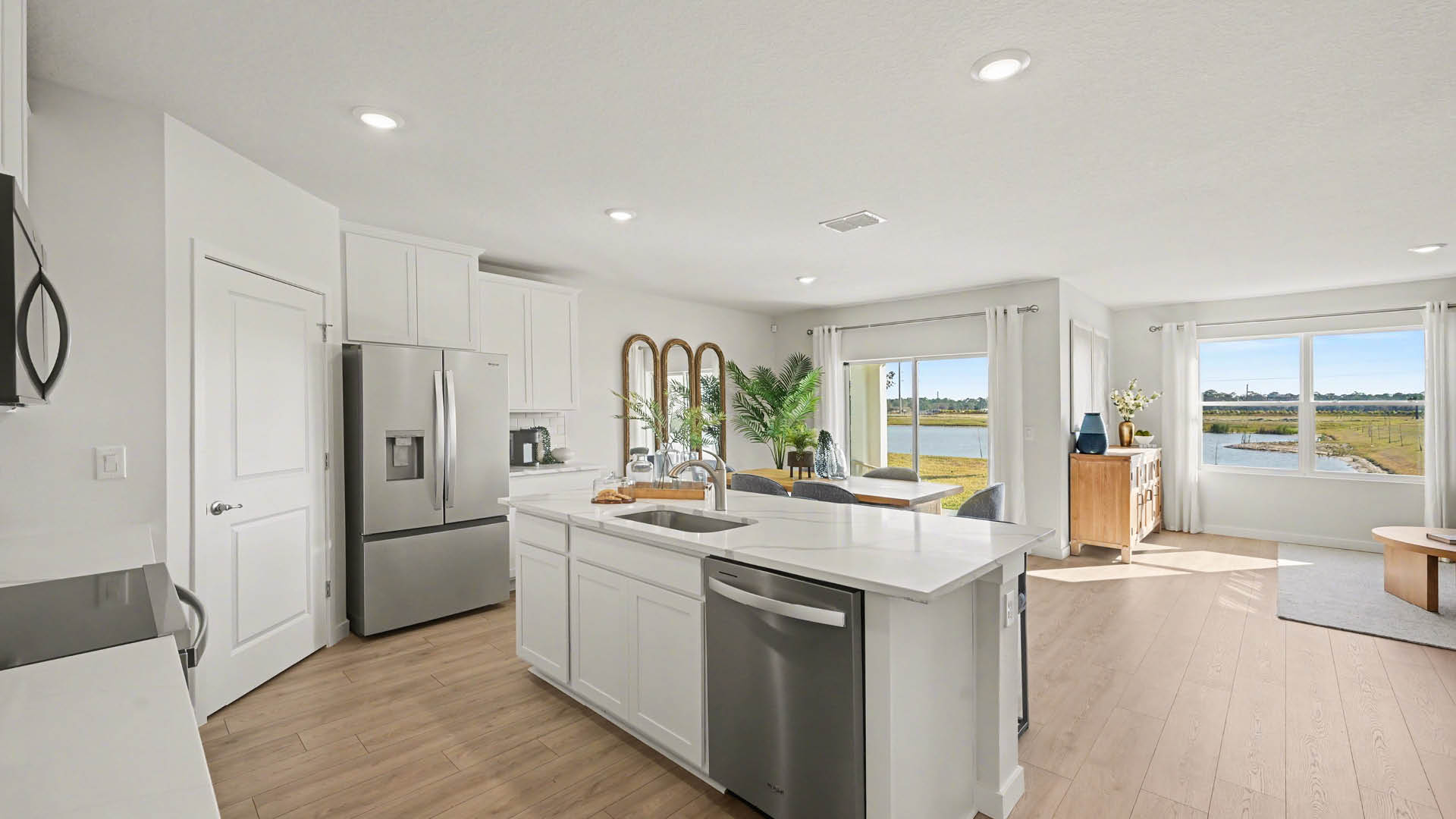 Bright modern kitchen featuring stainless steel appliances, sleek white cabinetry, and a center island. It features a sliding glass door and large windows, providing a view of the outdoors.